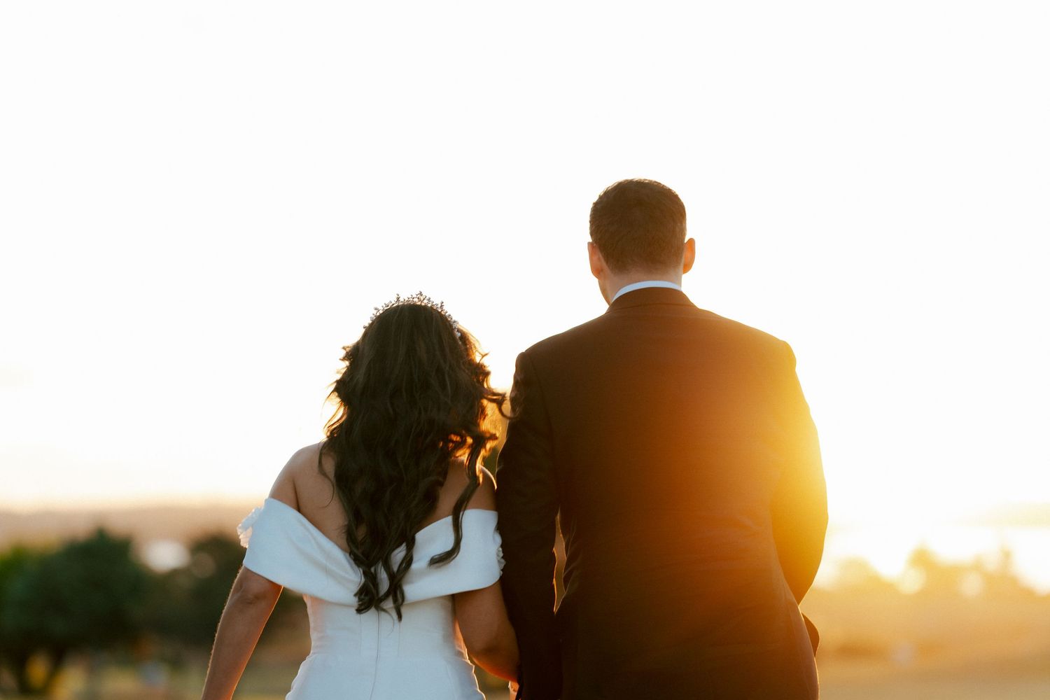 A couple watches the sunset together on their wedding day as golden light bathes them in warm tones.