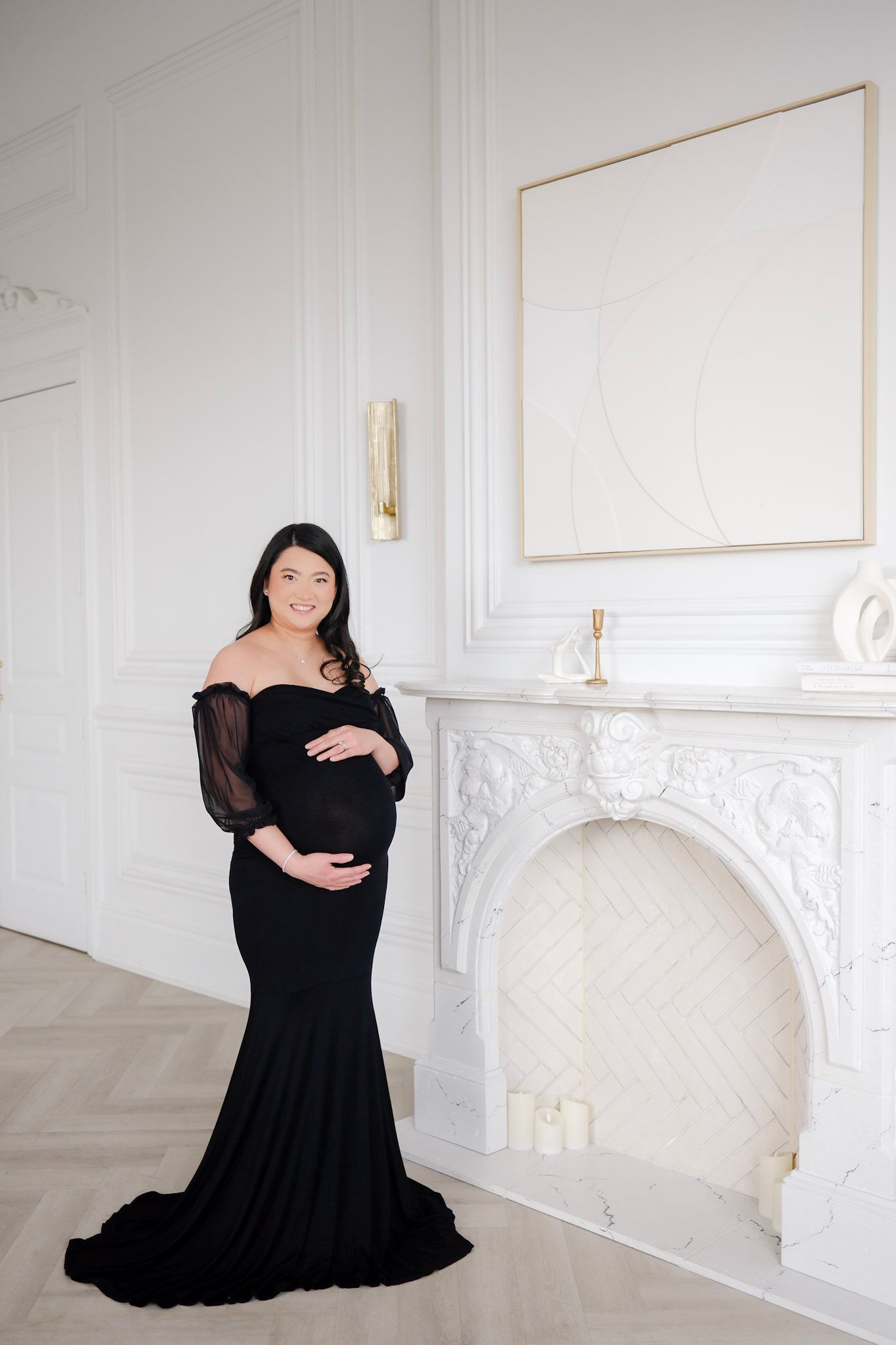 Elegant maternity photo session in a white room featuring a person in a flowing black dress posing gracefully.