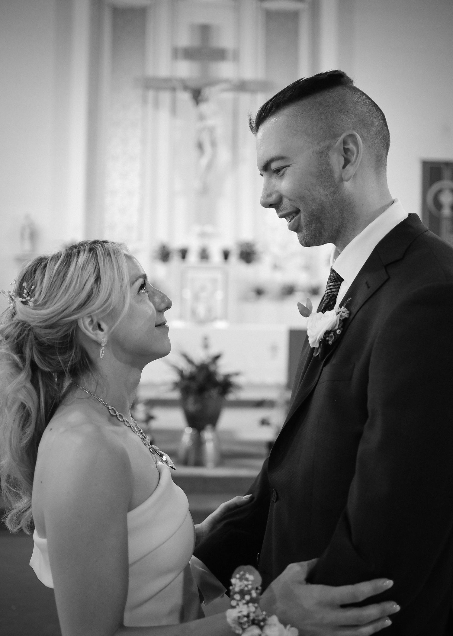 A romantic black and white moment between a bride and groom gazing at each other in a church setting.