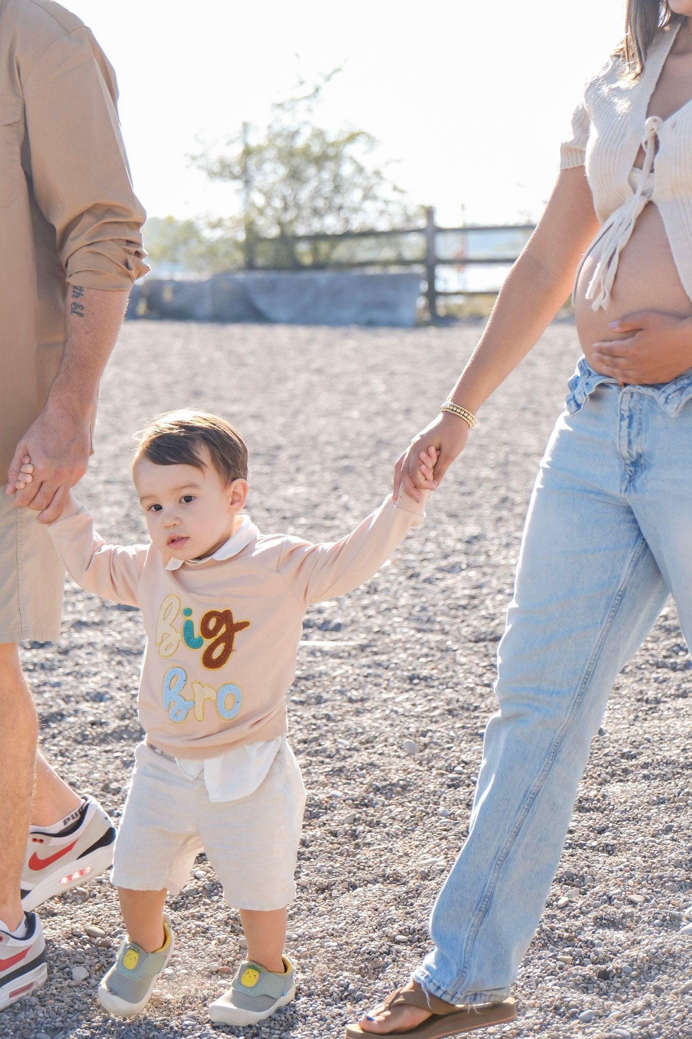 A row of legs in jeans and beige clothing stand together on rocky ground in natural sunlight.