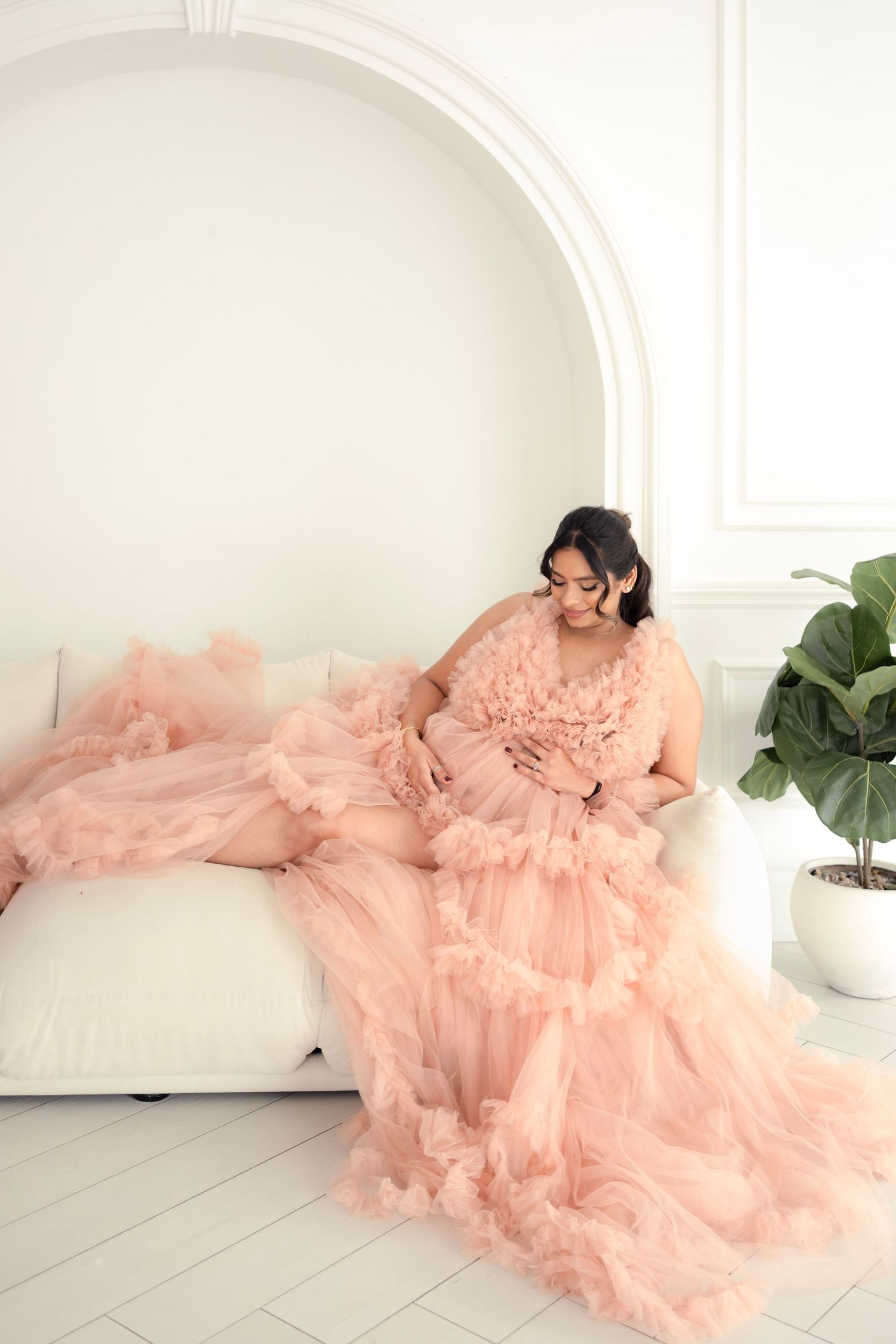 A flowing peach tulle gown drapes elegantly across a white chaise lounge in a bright minimalist setting.