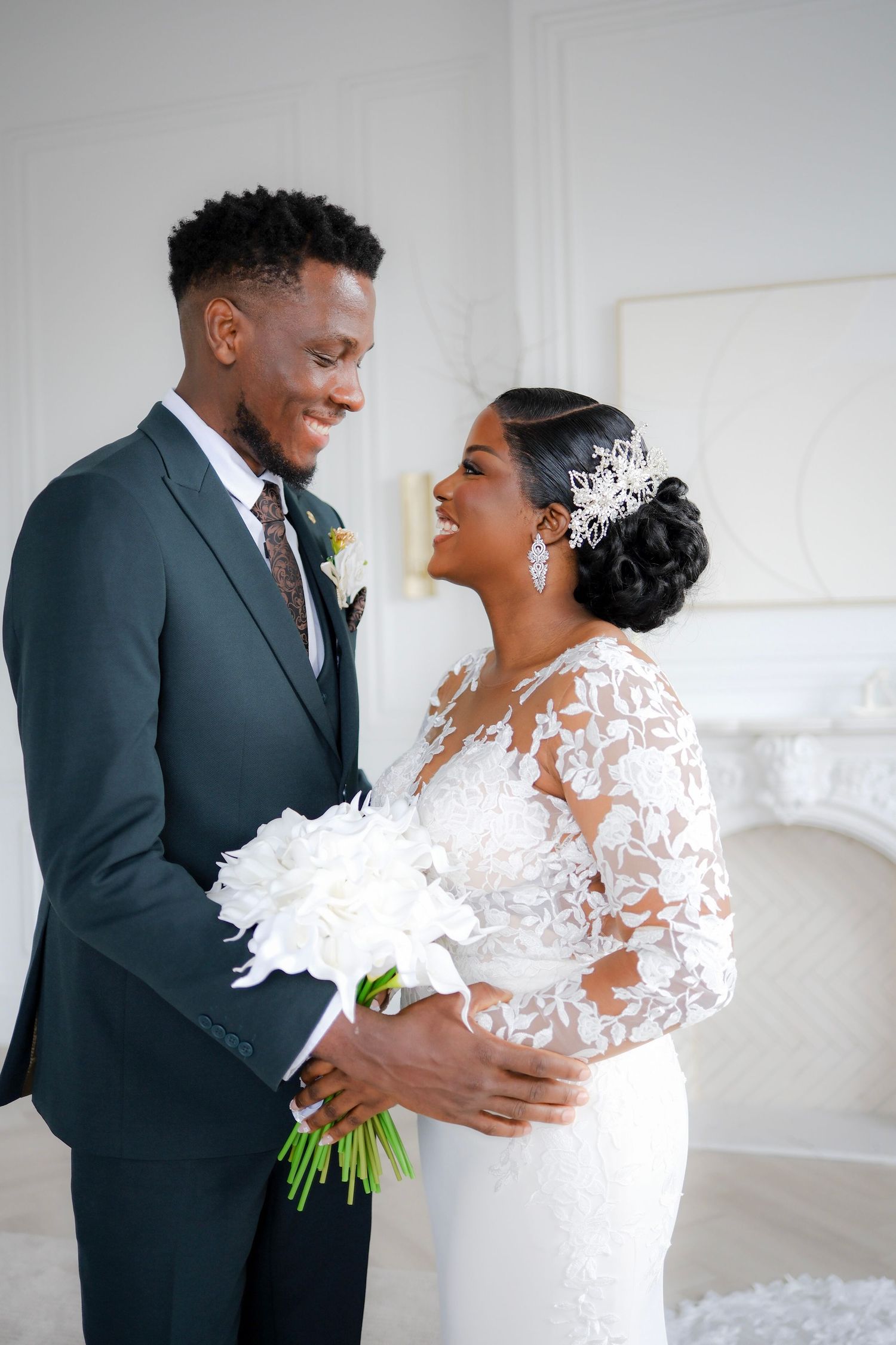 Joyful couple sharing a candid moment on their wedding day, bride in lace gown and groom in charcoal suit with white bouquet.
