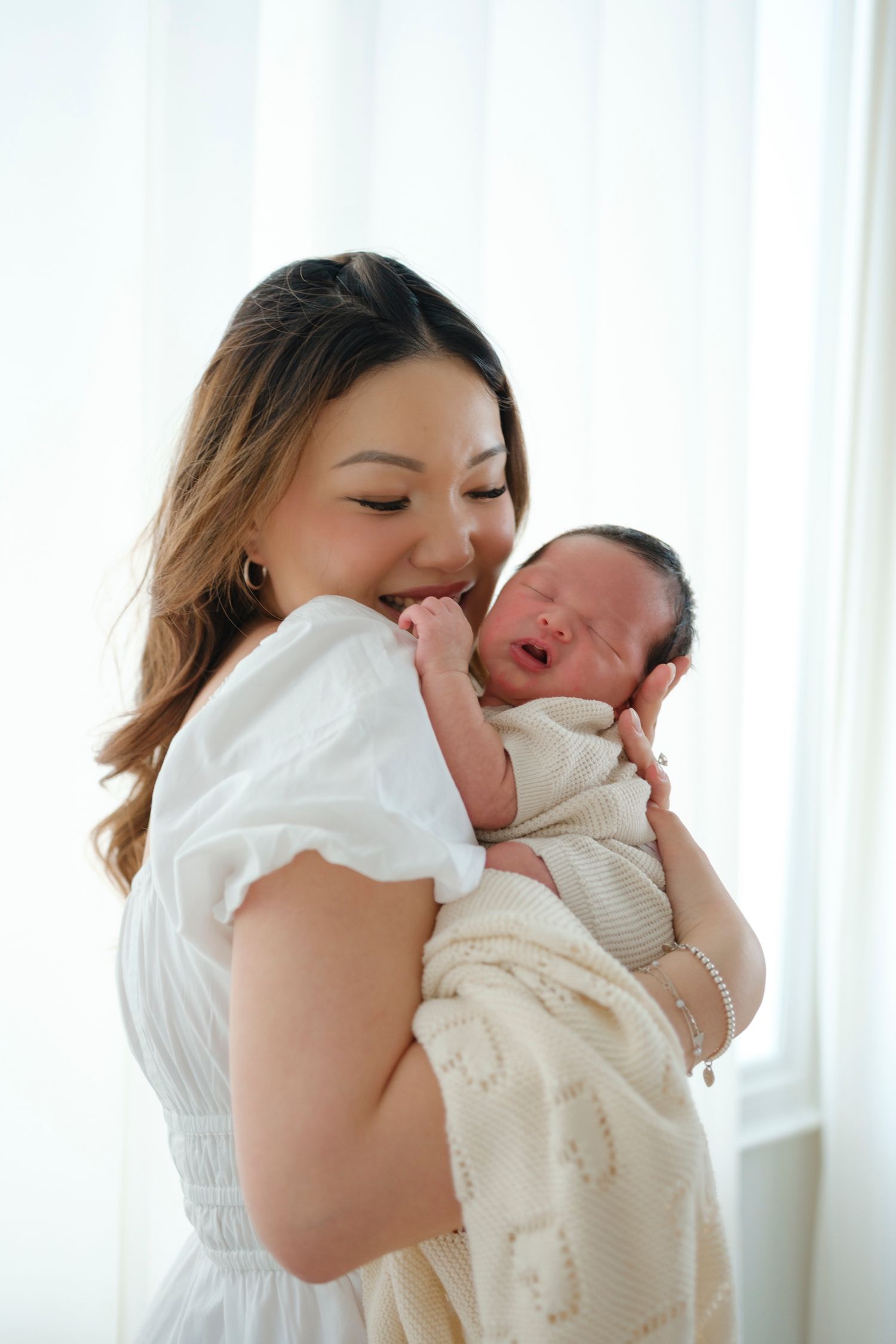A tender moment between mother and newborn baby against a bright white background.
