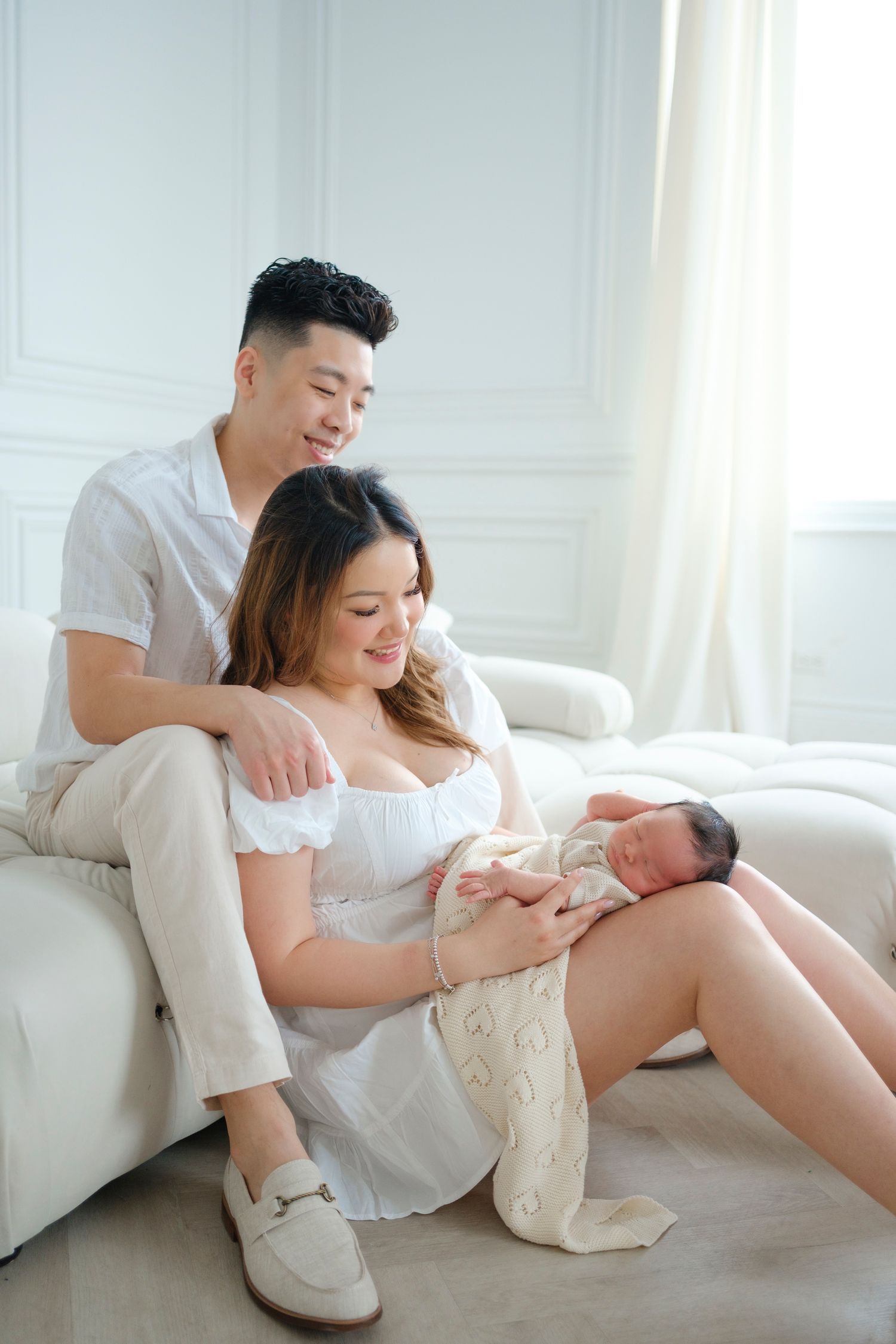 Family shares an intimate moment on white couch as new parents hold their newborn baby.
