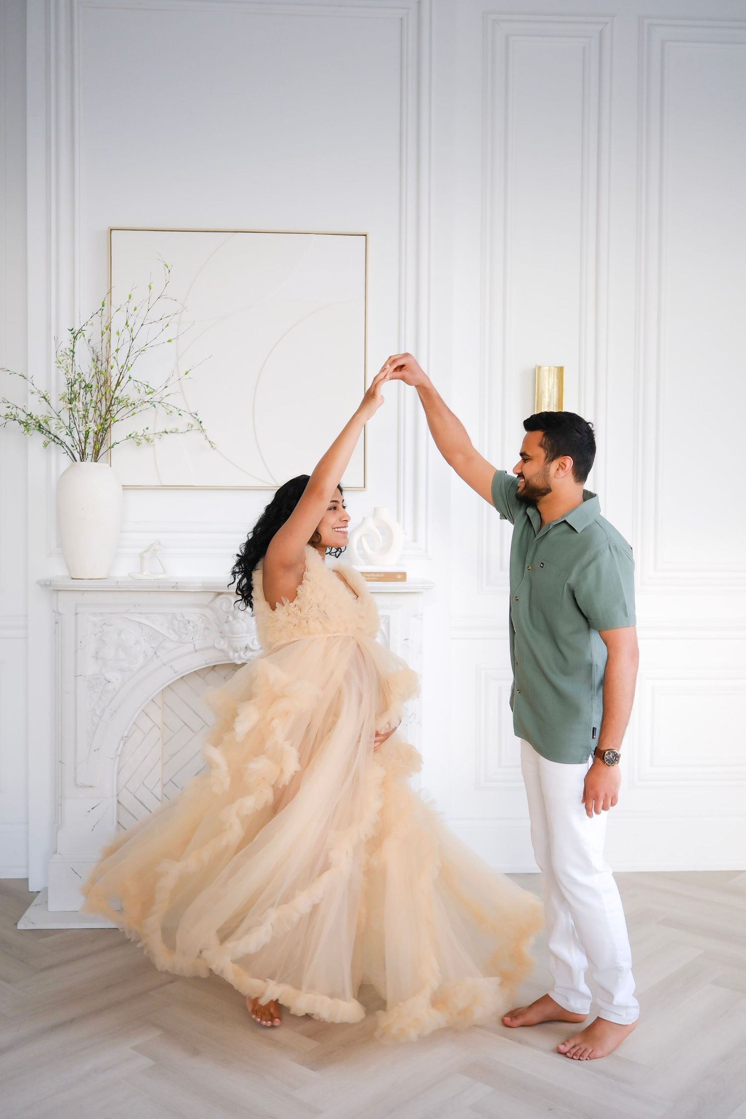 Couple dancing together in a bright white room, with the woman wearing a flowing champagne-colored gown and twirling gracefully.