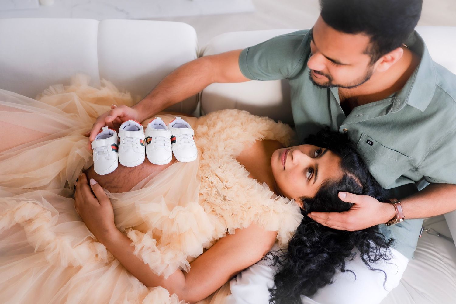 A couple in formal dress relaxes on a couch with small shoes and a tulle dress creating a romantic moment.