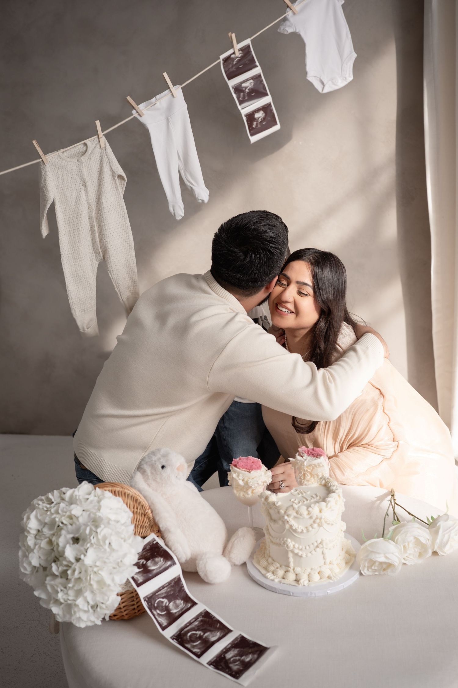 A pregnancy announcement photo series with ultrasound photos, baby clothes on clothesline, and white cake decorations.
