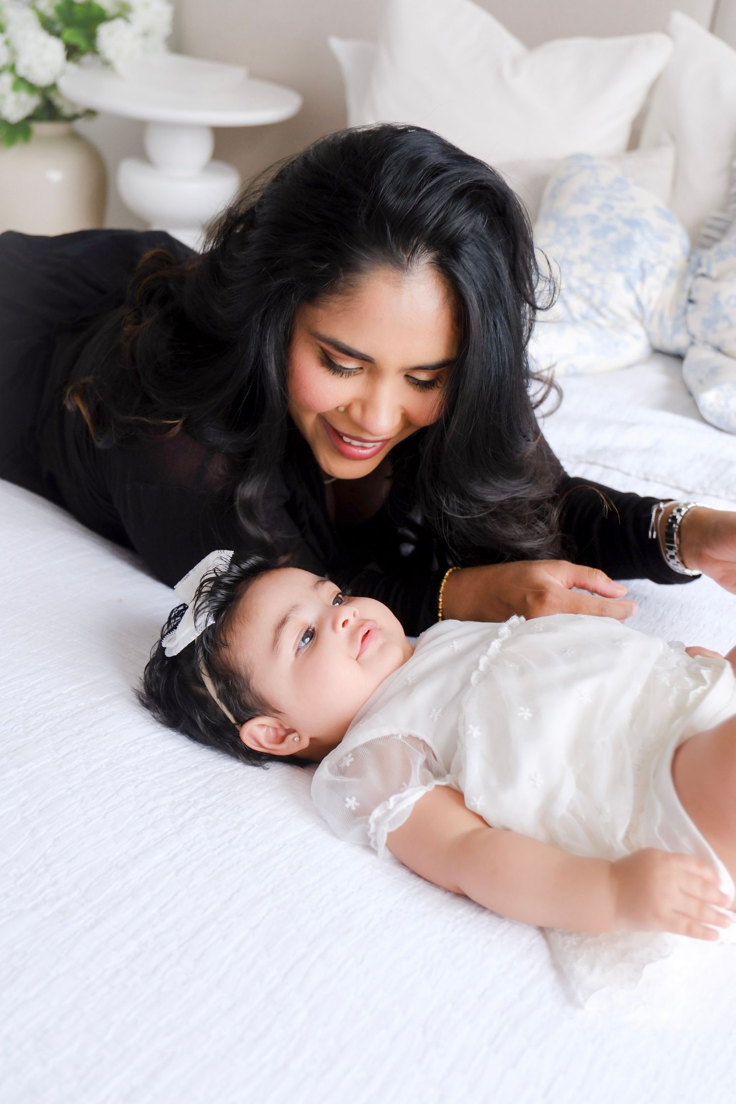 Mother and baby sharing a tender moment while lying together on white bedding.