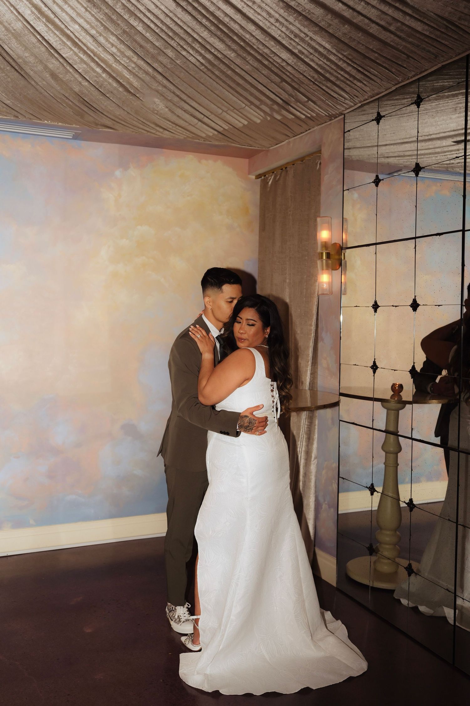 A couple shares an intimate dance moment at their wedding reception in a romantic venue with string lights and wooden ceiling.