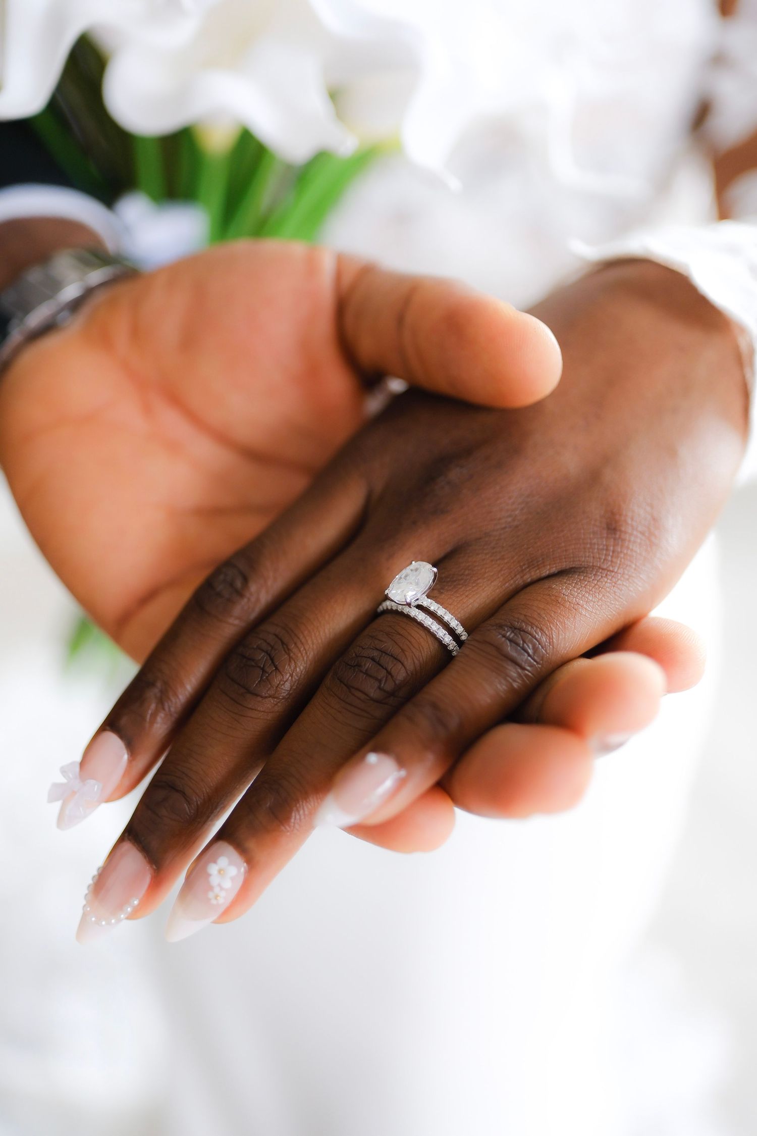Close-up detail of sparkling diamond engagement and wedding rings on hands against a light background.
