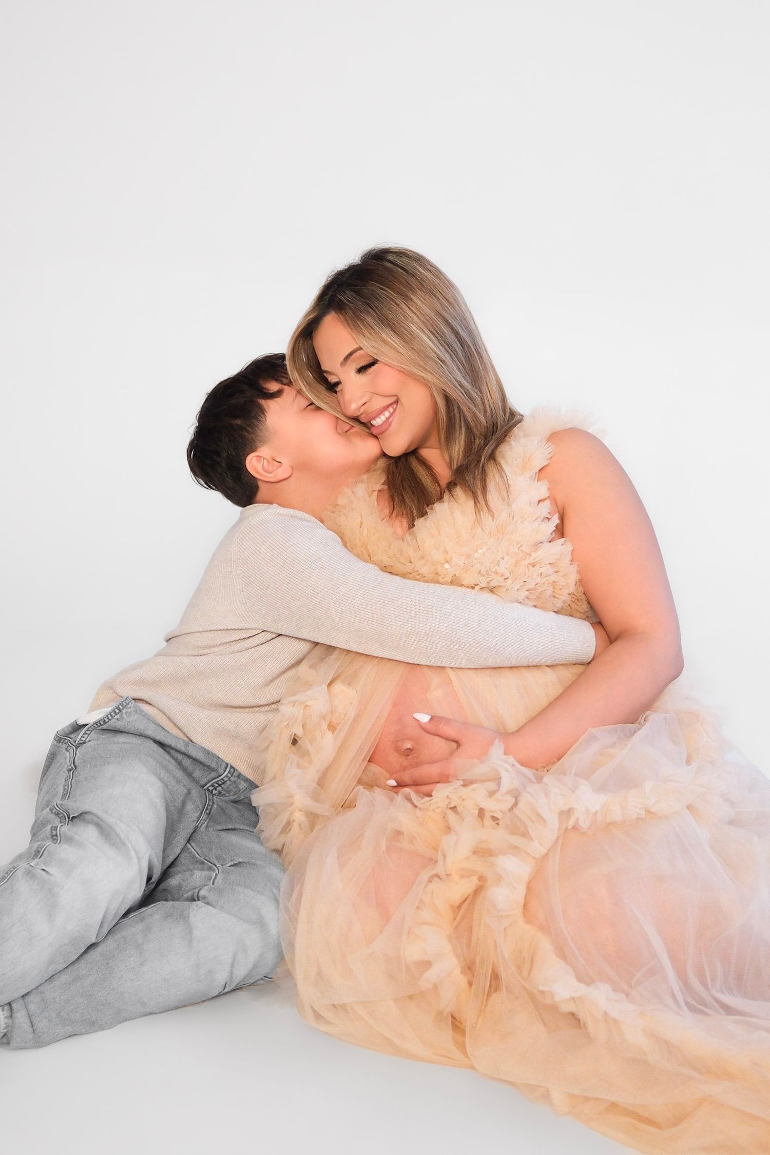 A tender moment shared between two people, one wearing jeans and the other in a flowing peach-colored tulle dress.