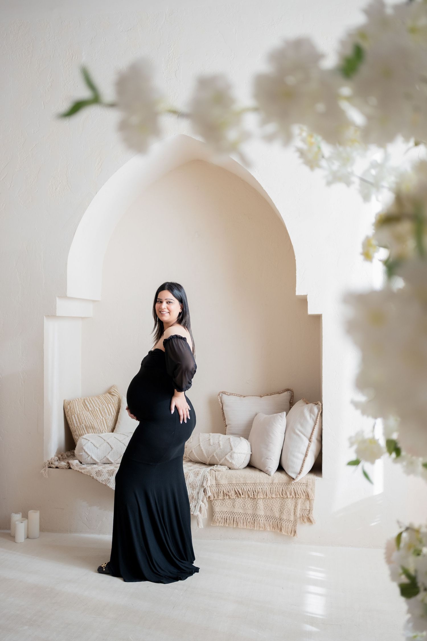 Elegant black dress silhouette against white arched alcove with plush seating and delicate floral decor.