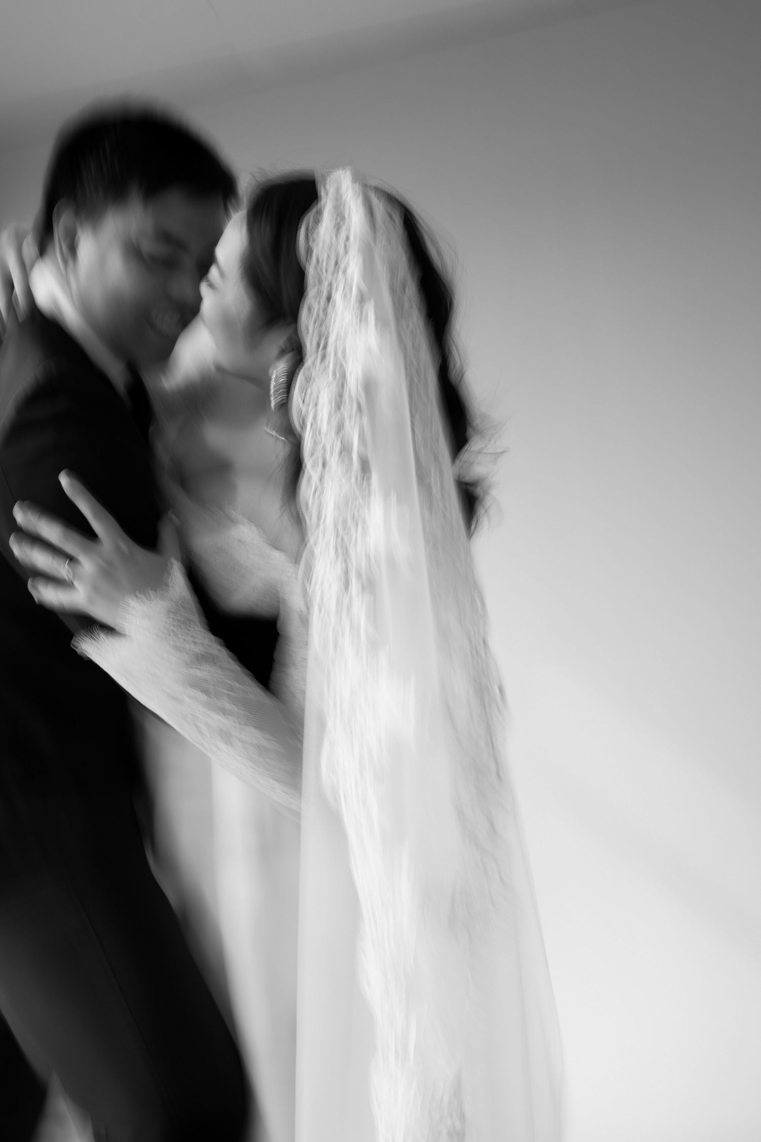 Blurred black and white photo of a bride and groom sharing a kiss, with lace veil cascading down.