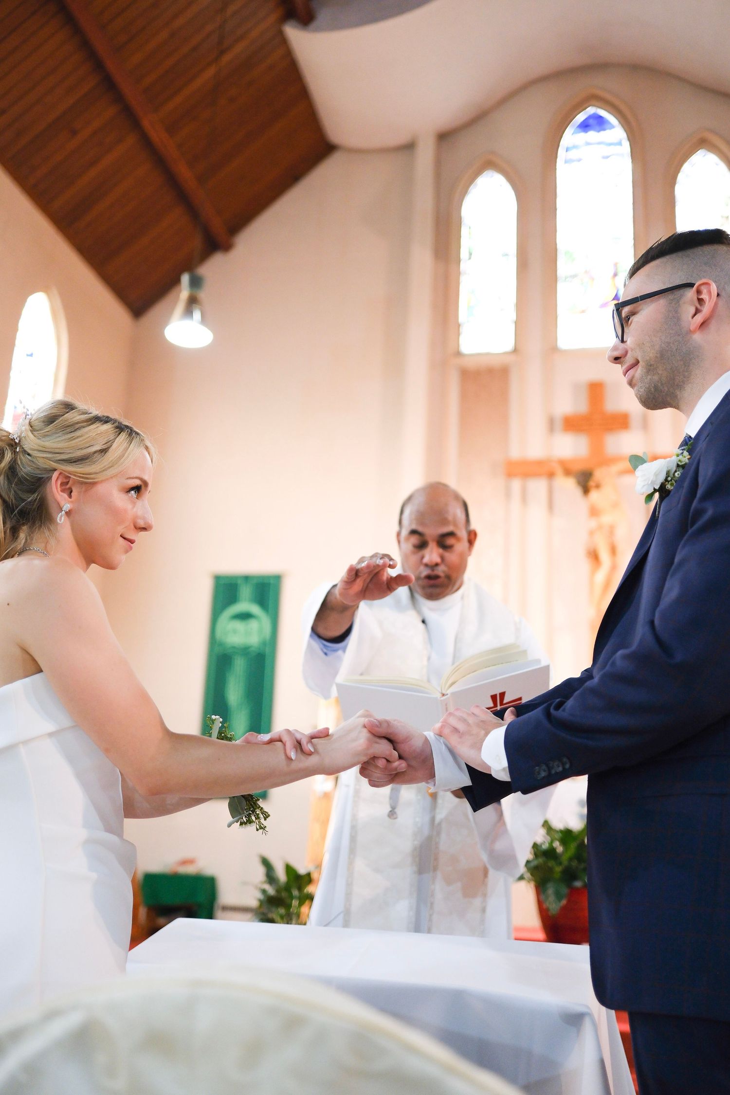 Wedding ceremony taking place inside a church with arched windows and wooden vaulted ceiling.