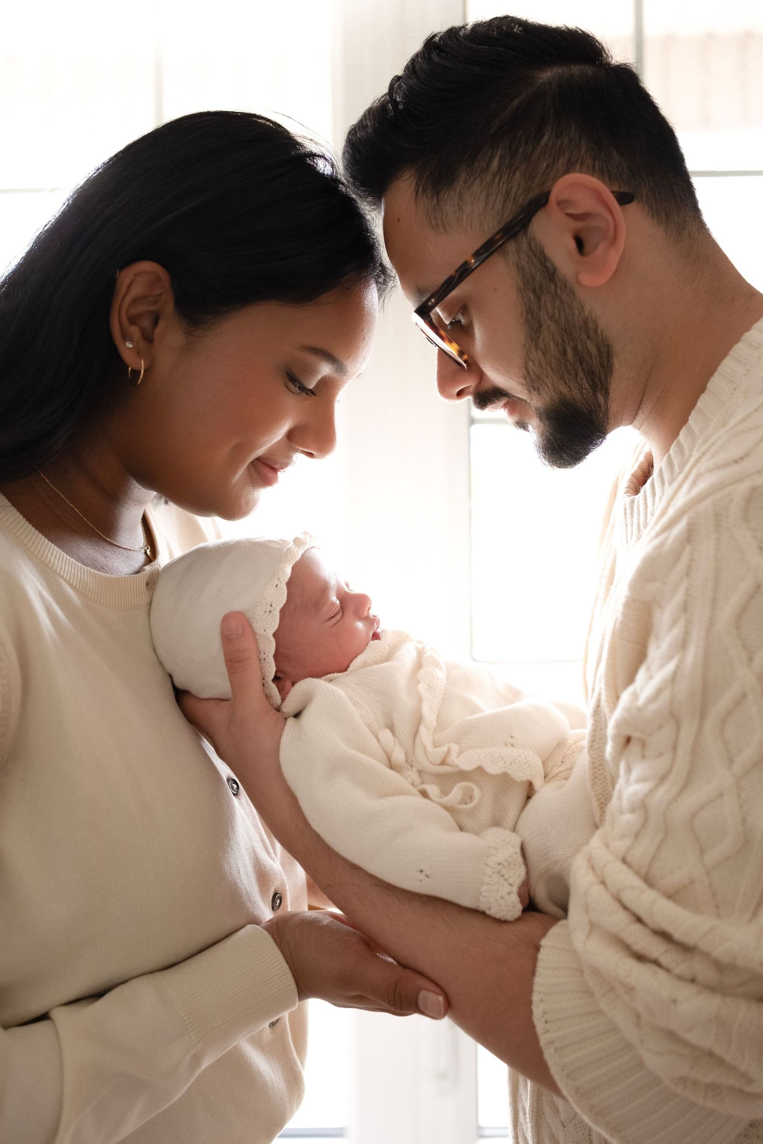 New parents lovingly cradle their sleeping newborn baby dressed in white, sharing a tender family moment.