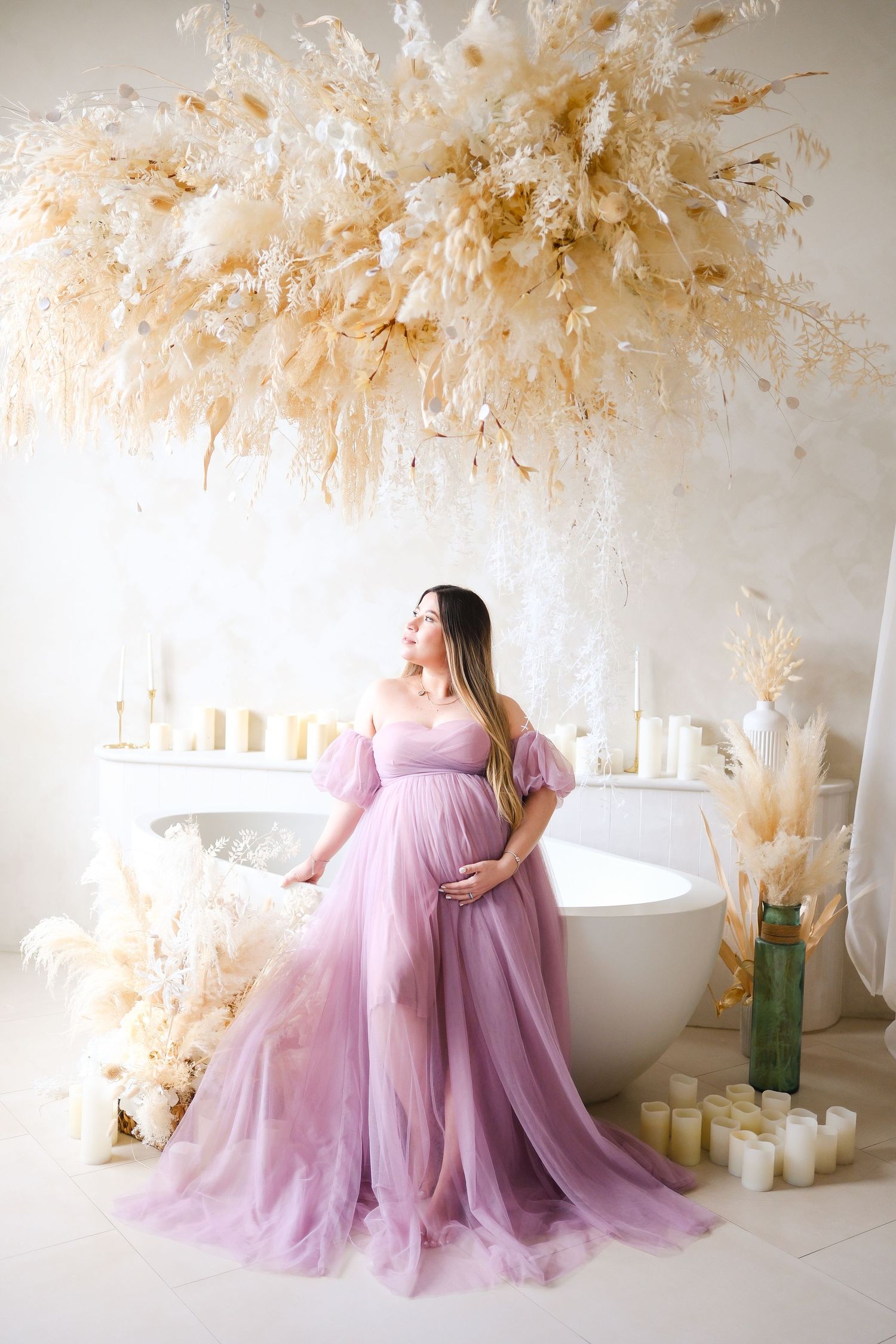 Ethereal maternity photo with woman in purple gown surrounded by candles and dried flowers.