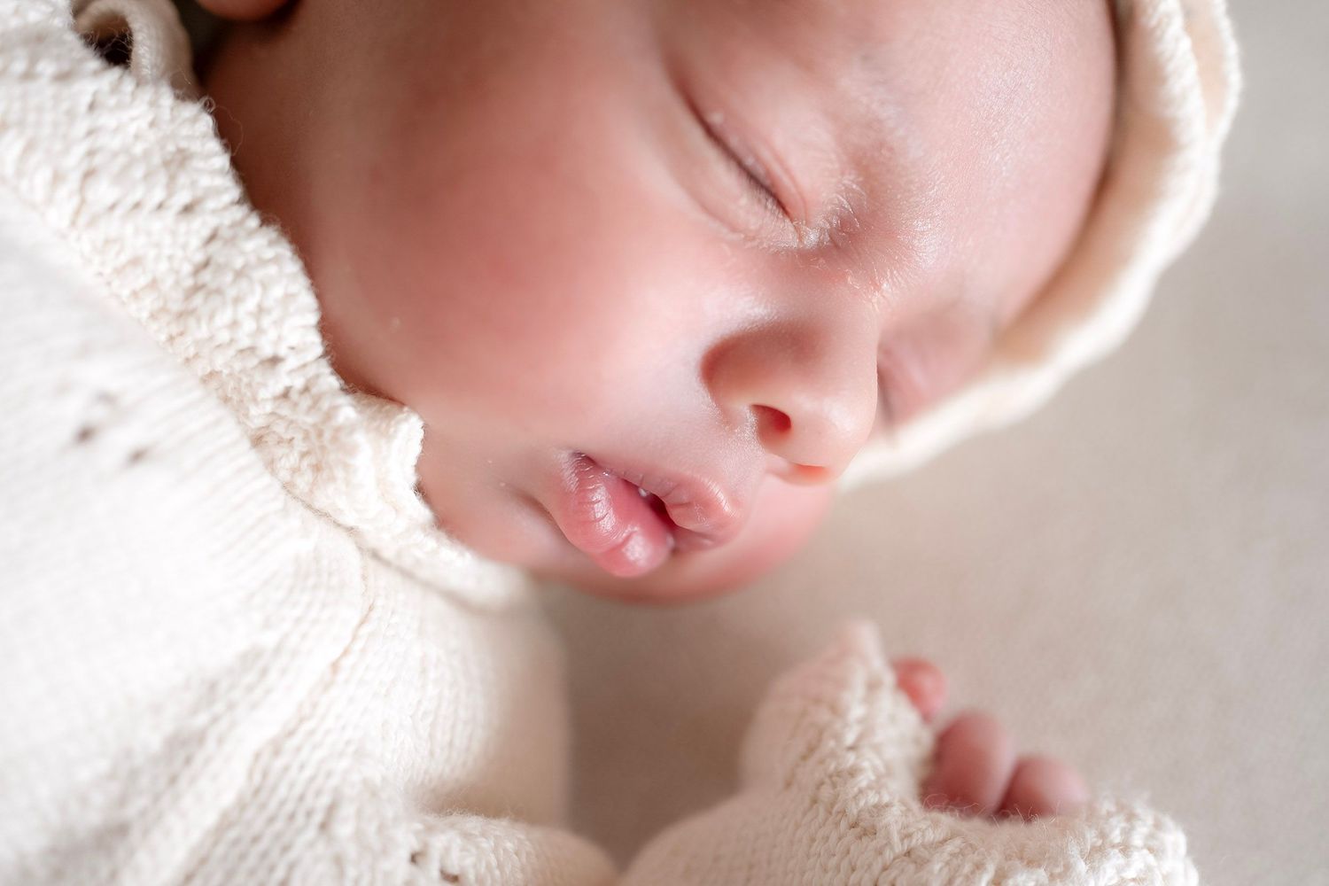 Peaceful newborn baby sleeping in a white knit bonnet and outfit, close-up portrait photography.