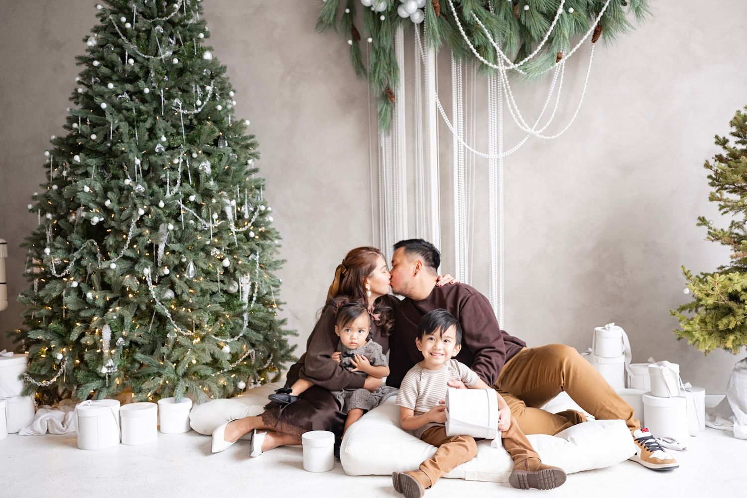 Romantic couple lying on floor beside Christmas tree in cozy white room during intimate holiday photoshoot.