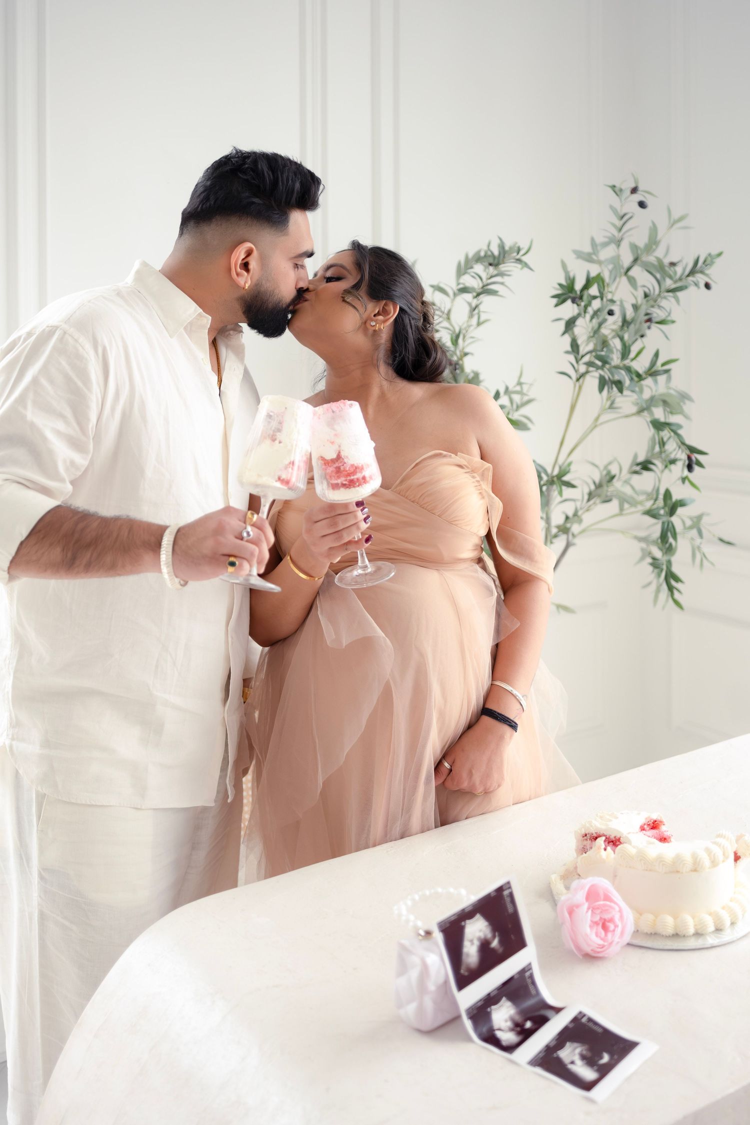 Celebration scene with champagne toast, ultrasound photos, and pink cake in bright white room.