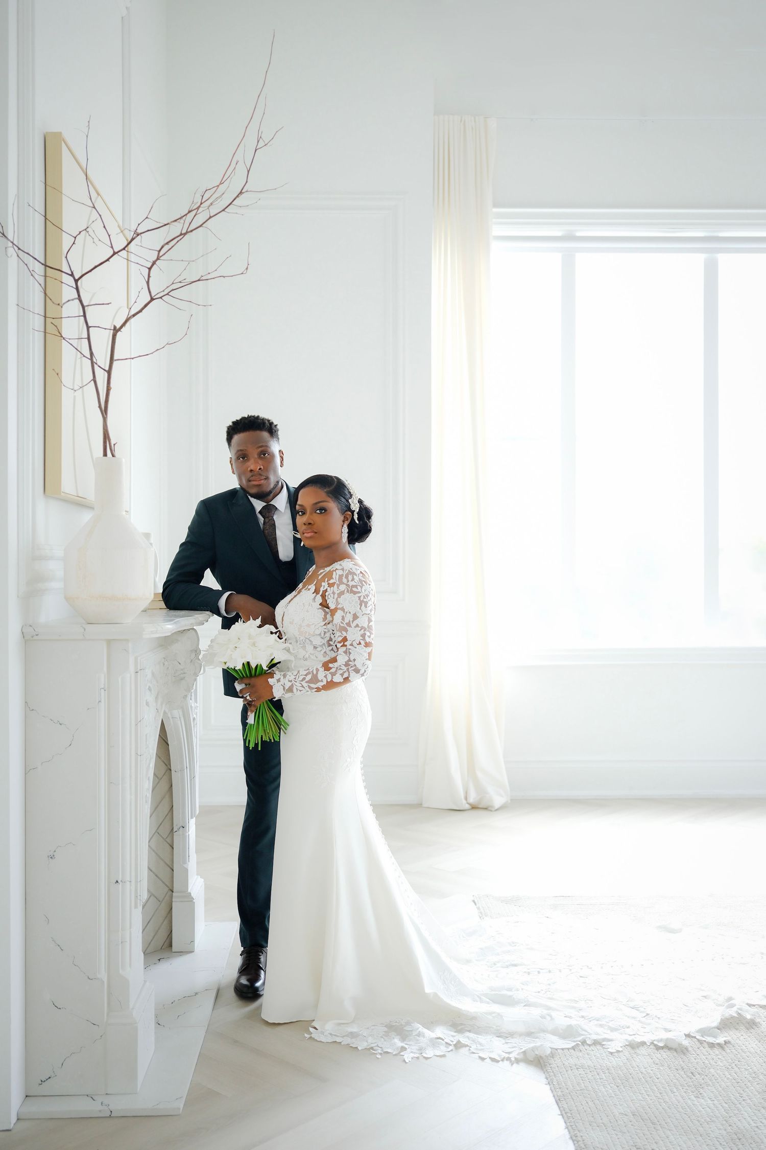 A romantic wedding portrait near a white fireplace shows a couple in elegant attire with a long lace gown and bouquet.