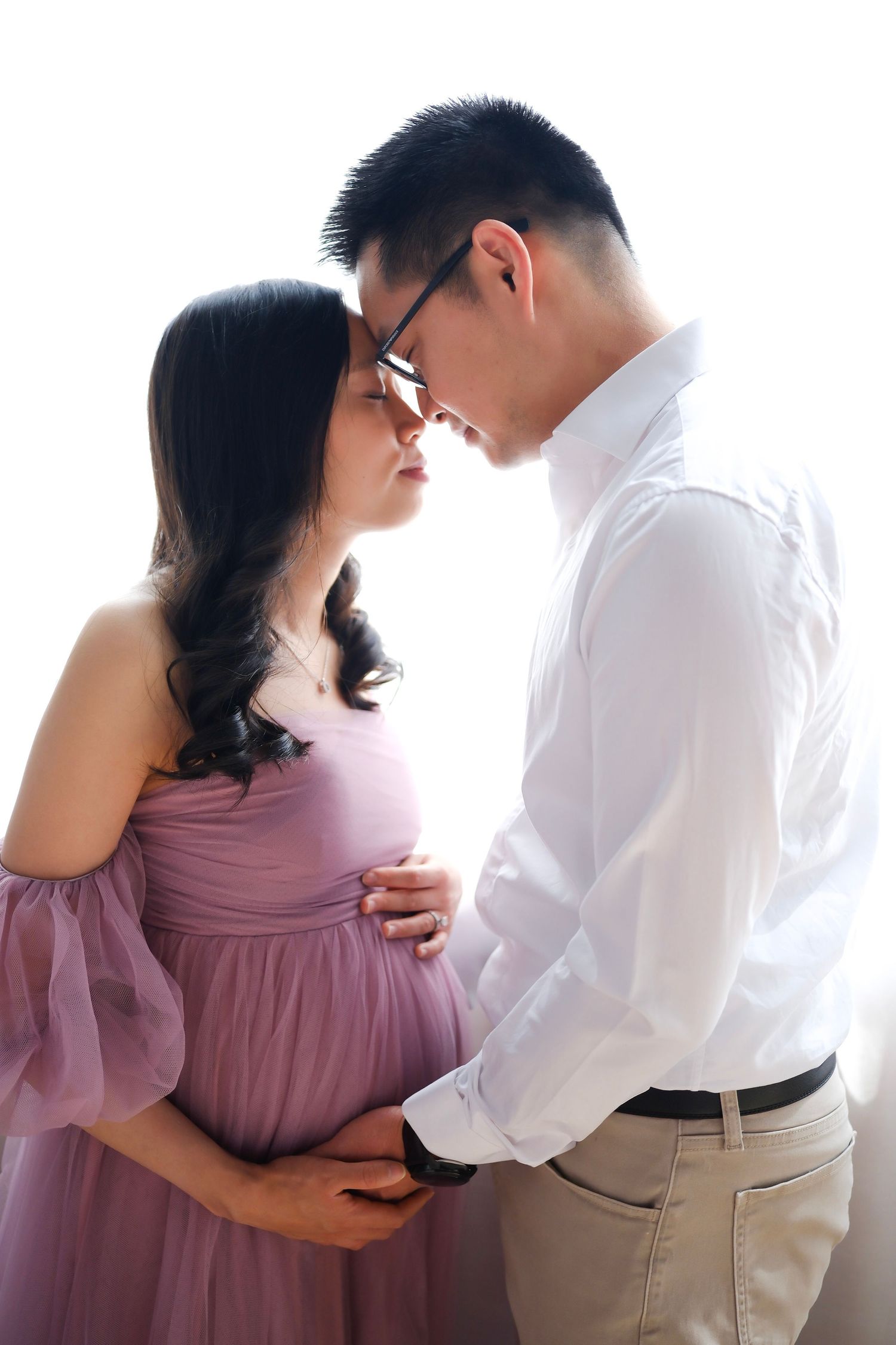 Elegant maternity portrait with woman in flowing pink dress against soft lighting.
