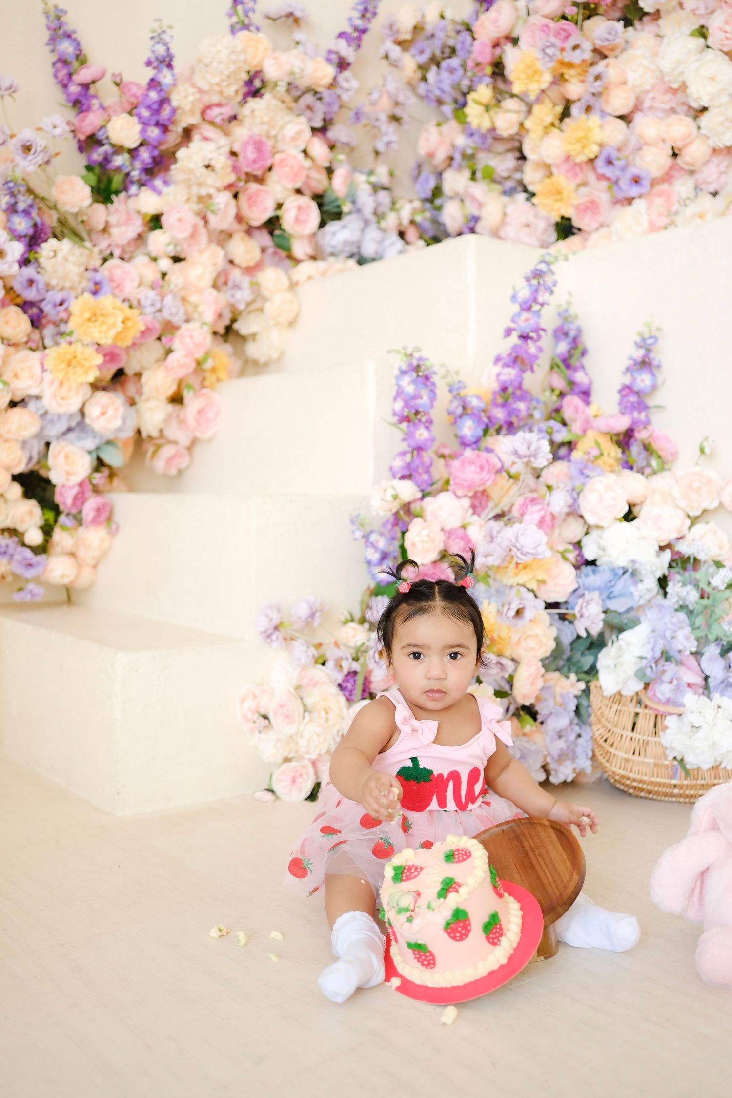 Beautiful pastel floral backdrop with delphinium and roses frames a spring photo shoot setting with plush toys.