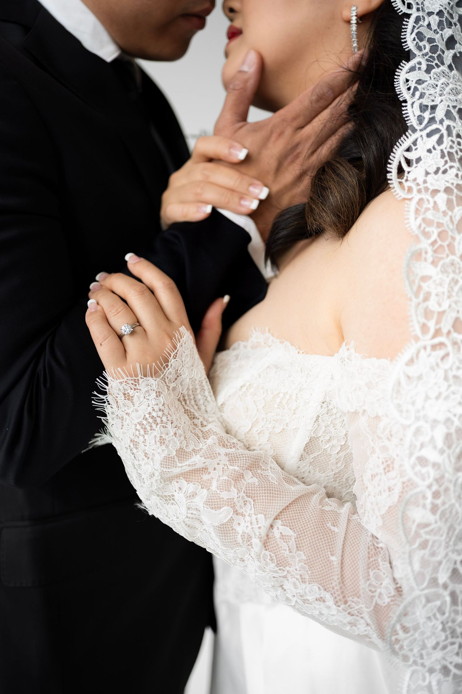 Close-up of bride and groom embracing, showcasing diamond engagement ring and lace wedding dress.