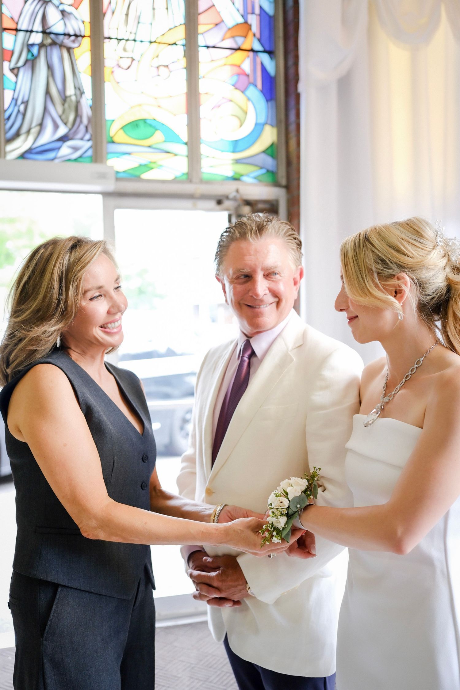 A wedding ceremony takes place near a stained glass window as three people gather for an intimate celebration.