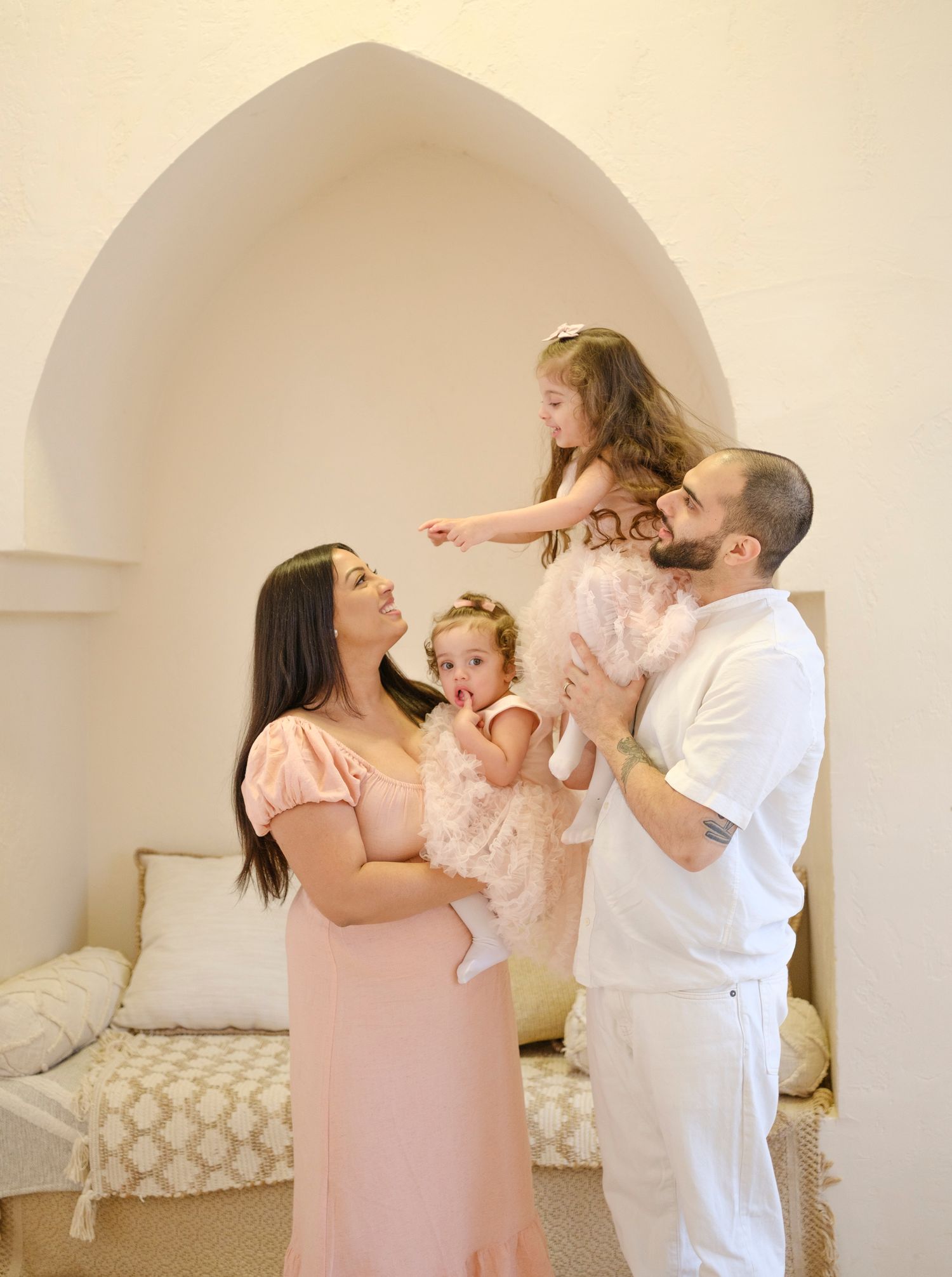 A family in matching pink and white outfits shares a joyful moment together in front of an arched wall.