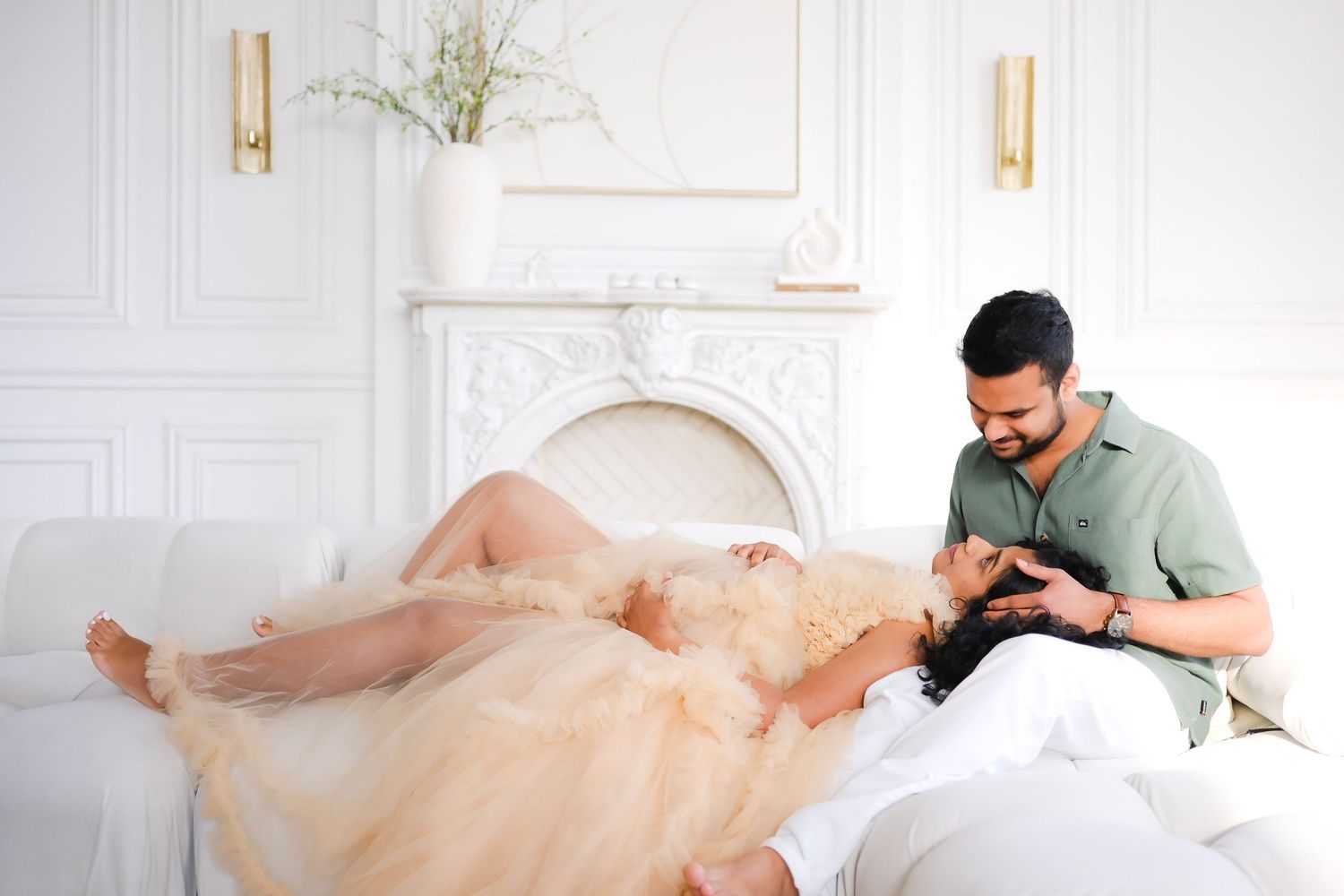 A person in a mint green shirt pets a golden retriever dog laying on a white couch in an elegant white room.
