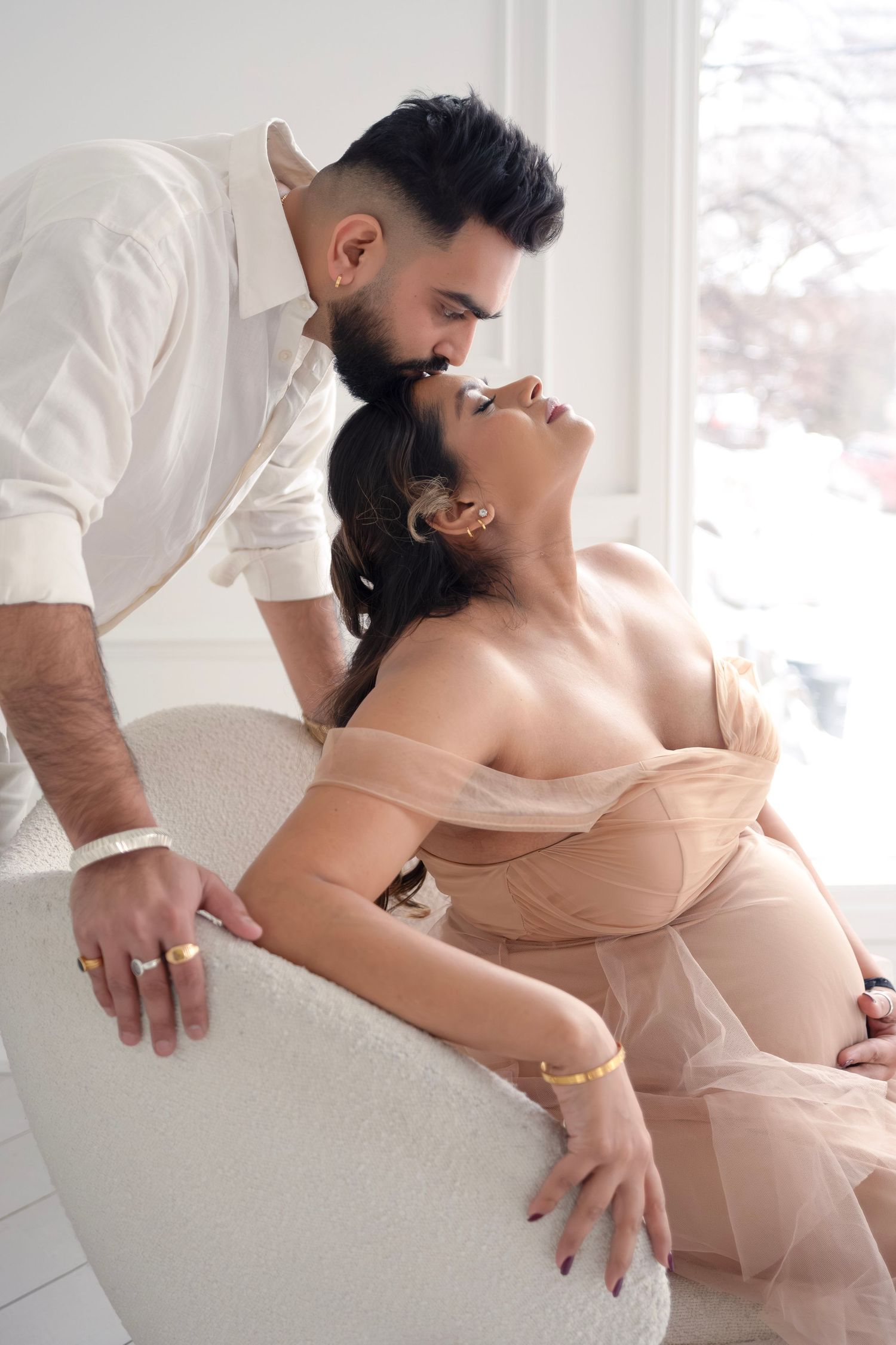 A series of intimate maternity photos showing a couple embracing in soft natural light by a window.