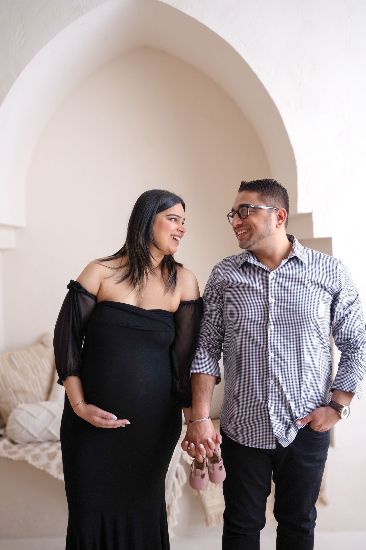 A couple in black and gray outfits poses playfully in a series of four romantic photos against a white arched wall.