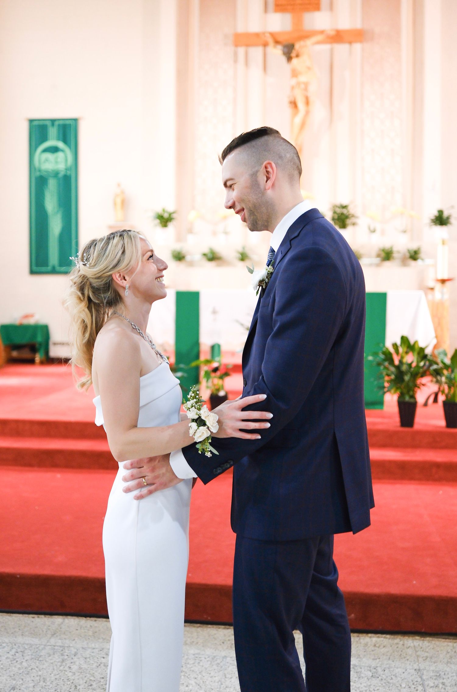 A bride and groom share an intimate moment inside a church with red carpet and crosses in the background.