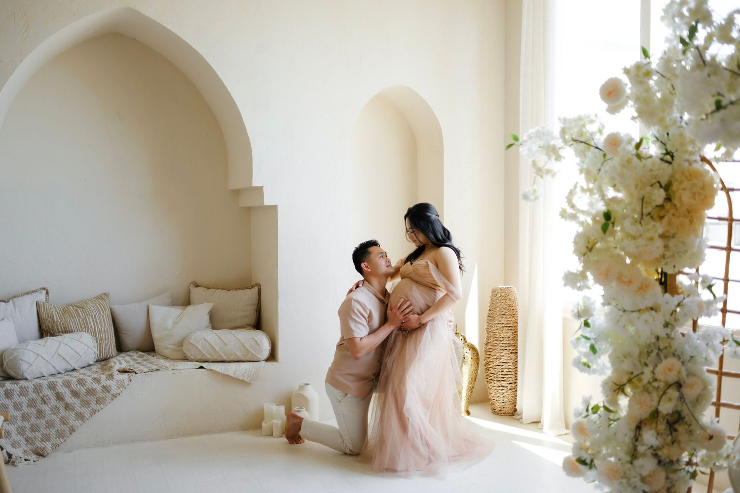 Couple sharing a romantic moment in a bright white studio with arched walls and elegant floral arrangements.