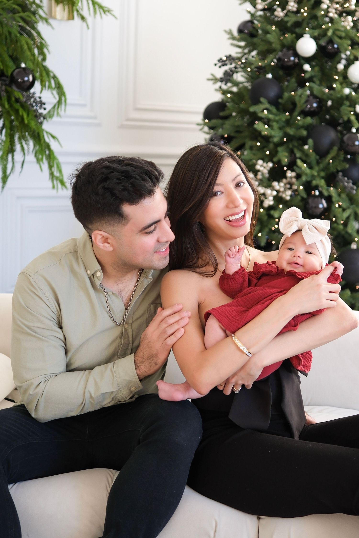 A couple shares playful and intimate moments while sitting on a white couch during a holiday photoshoot.