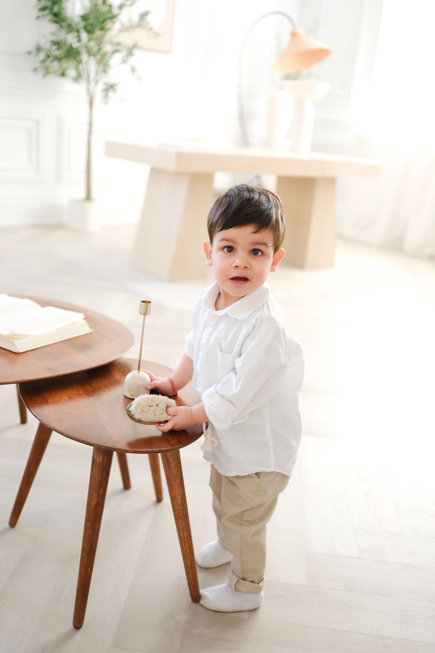 Small child in white shirt and khakis standing by wooden side table in bright room. Toronto, Greater Toronto Area, photographer
