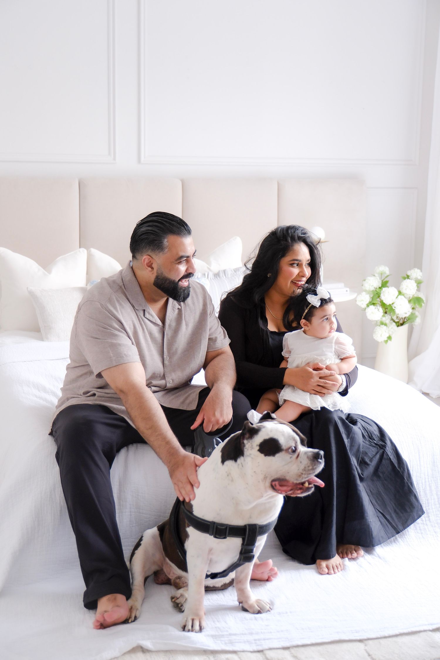 A family relaxes together on a white couch with their black and white pit bull dog and infant child.