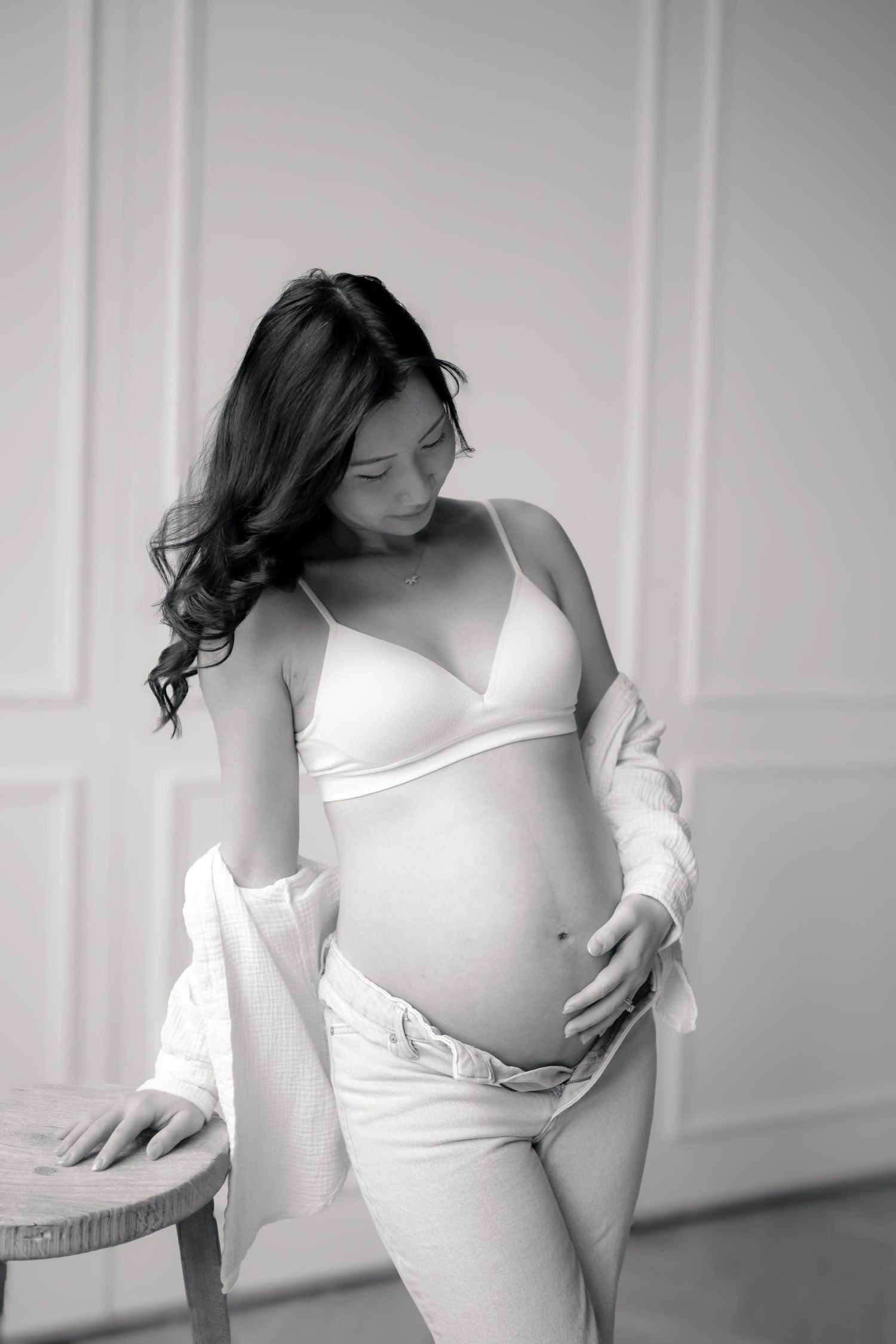 Black and white maternity photo of a pregnant woman in white lingerie and open robe, cradling her baby bump.