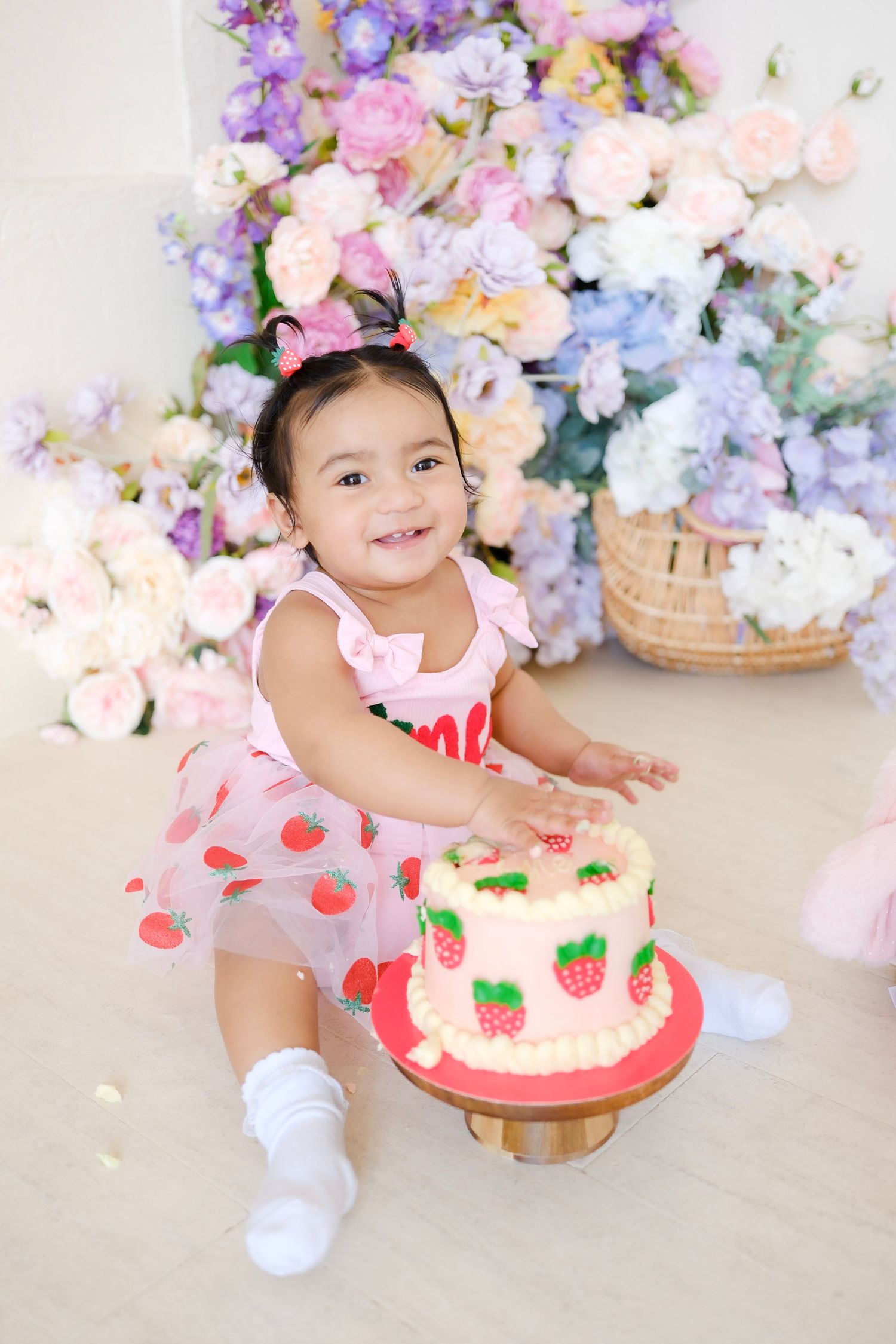 Sweet birthday celebration with strawberry cake and floral decorations in pink and purple tones against pastel backdrop.