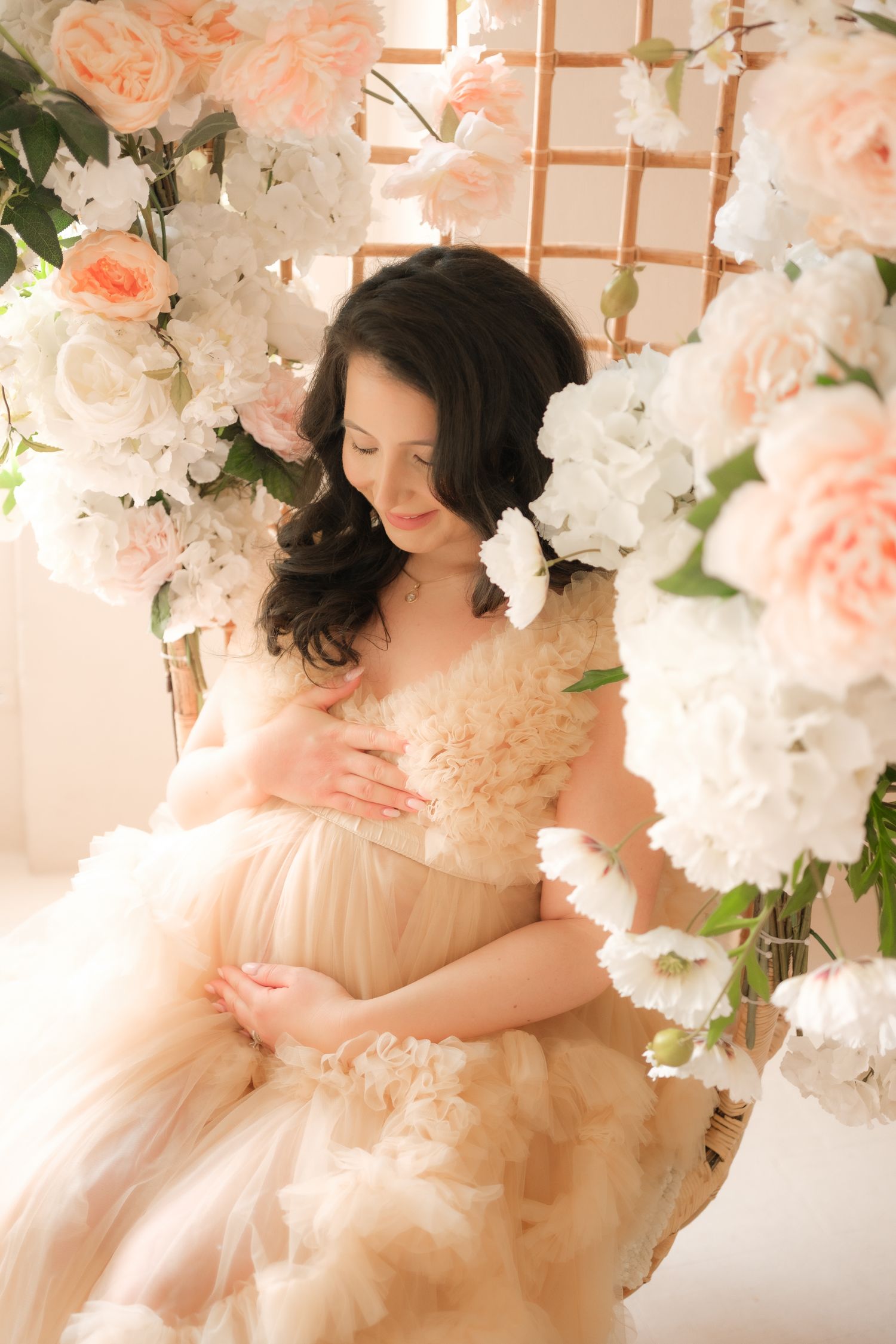 Romantic portrait in peach tulle gown surrounded by pink roses and white floral arrangements against lattice backdrop.