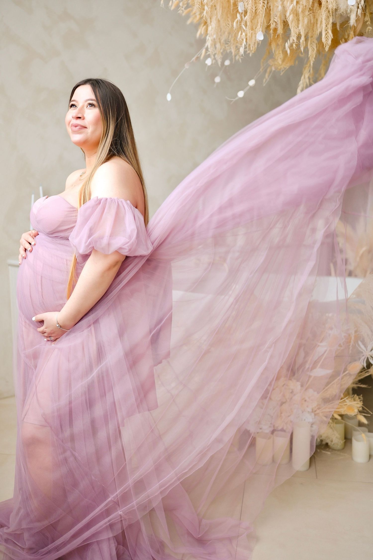 Dynamic maternity photo with flowing pink dress movement against neutral backdrop.