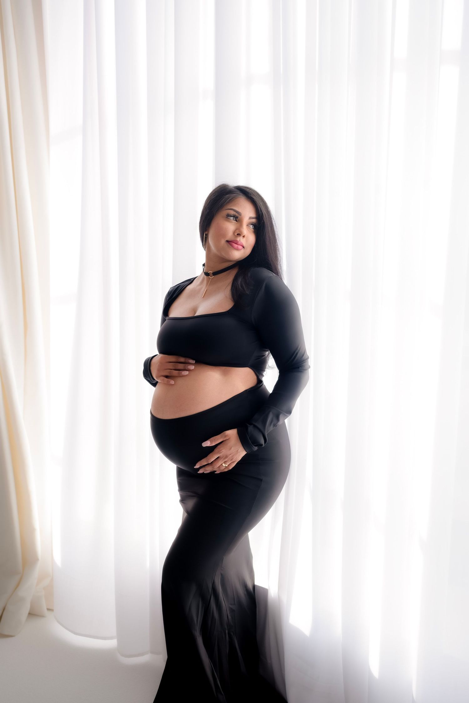 A series of four maternity photos showing a pregnant woman in a black dress against a bright window backdrop.