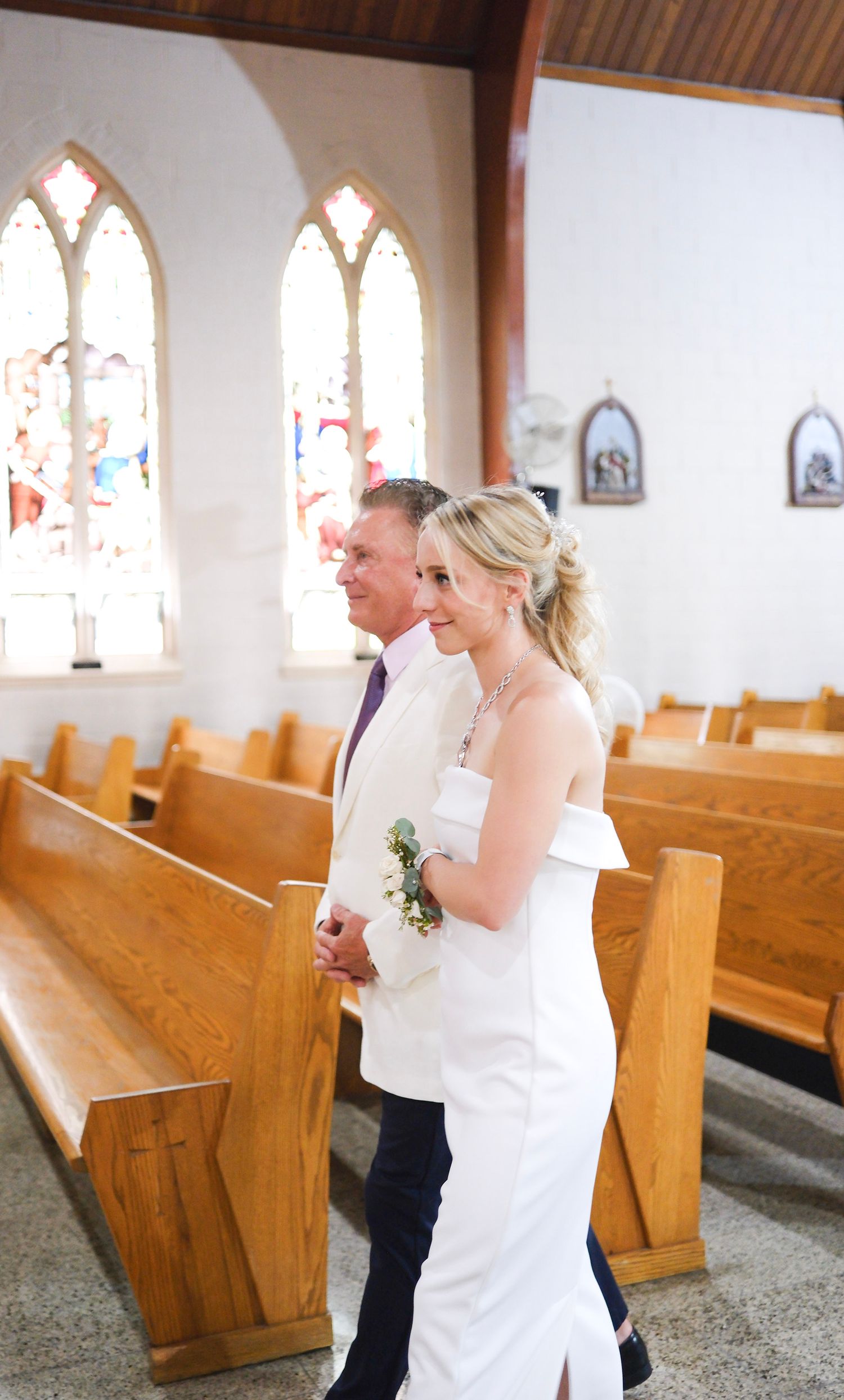 A serene moment in a chapel with wooden pews and Gothic arched windows during a wedding ceremony.