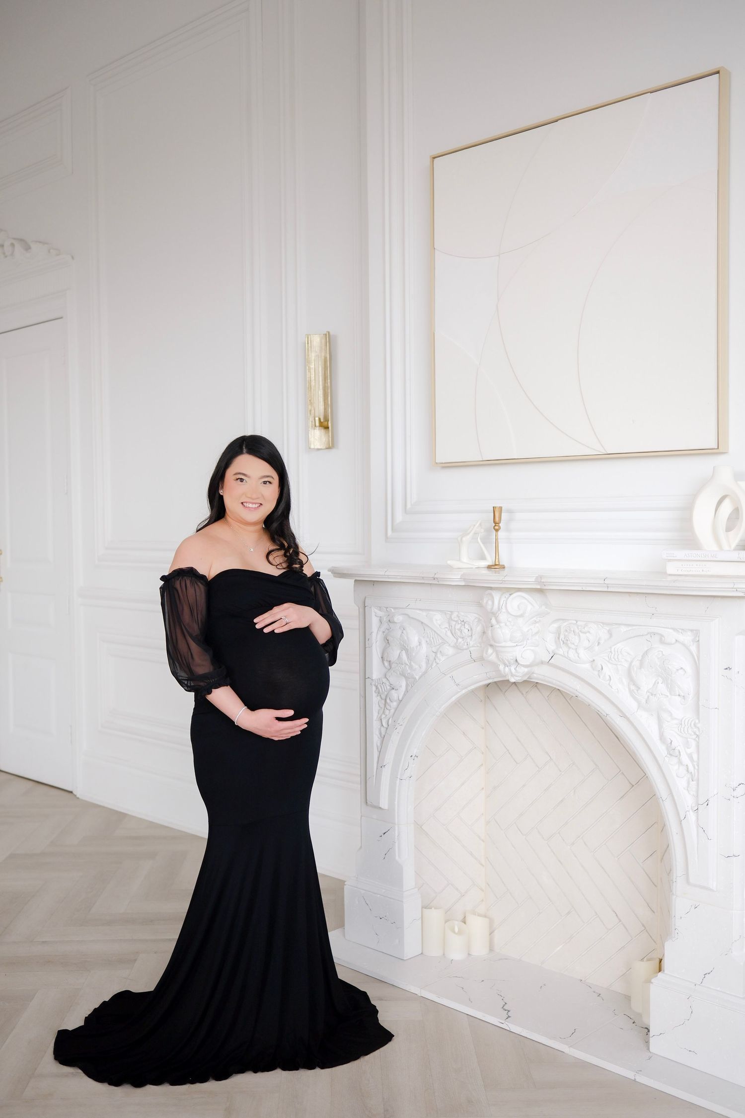 A person in a black dress poses gracefully in a bright white room with elegant molding and architectural details.