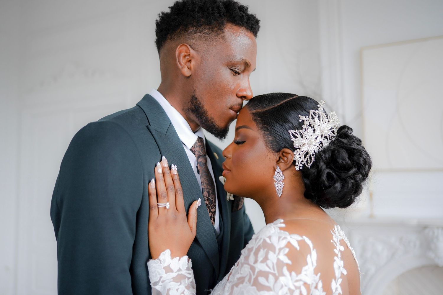 A romantic wedding portrait of a bride in lace and groom in navy suit sharing an intimate moment together.