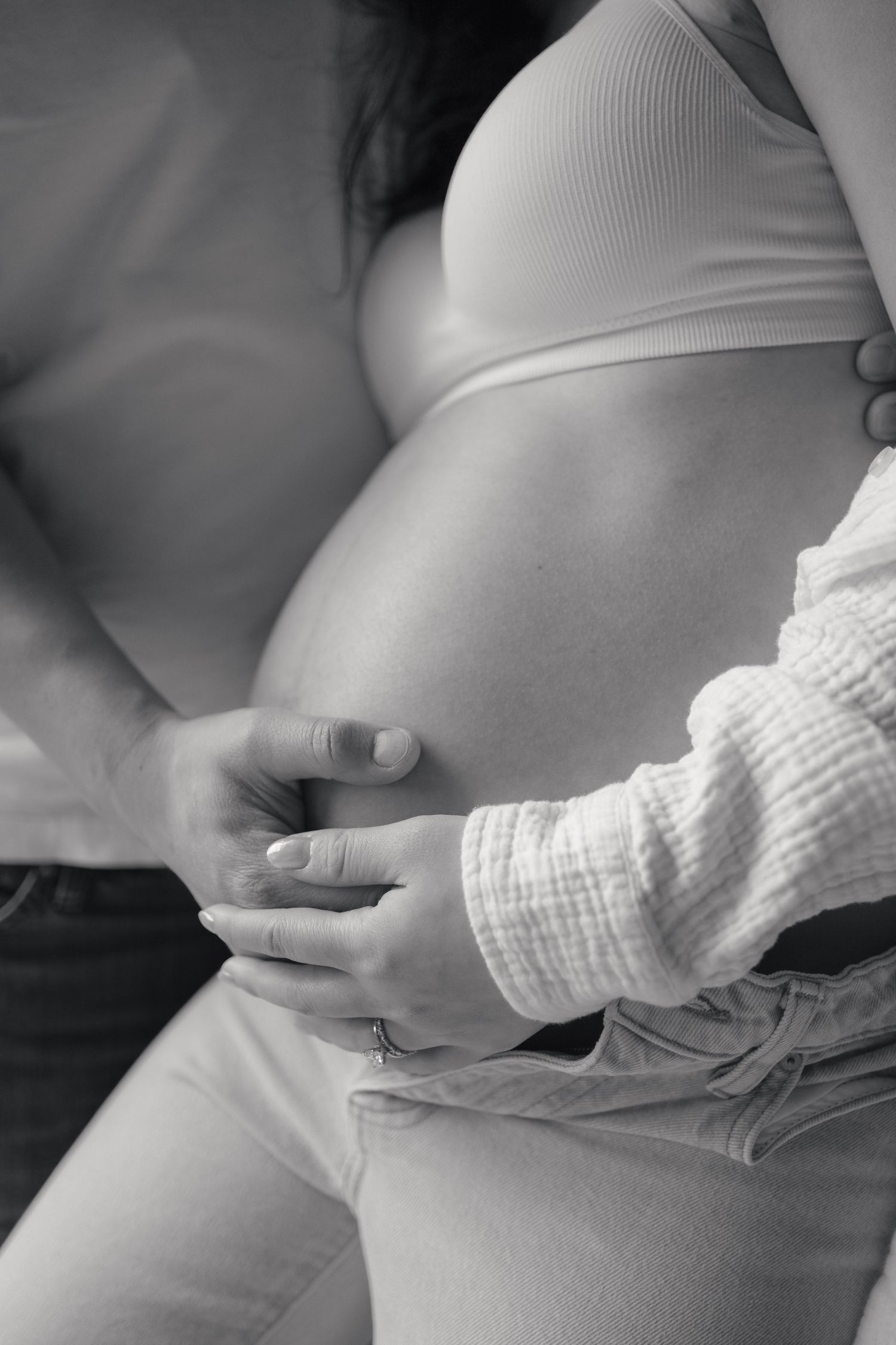 Black and white photo of a pregnant woman's belly with hands gently cradling it.