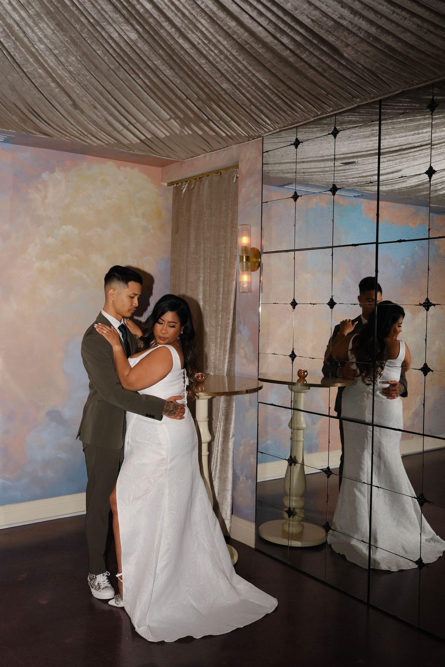 A newly married couple shares an intimate dance moment in a room with ethereal cloud-painted walls and string lights.
