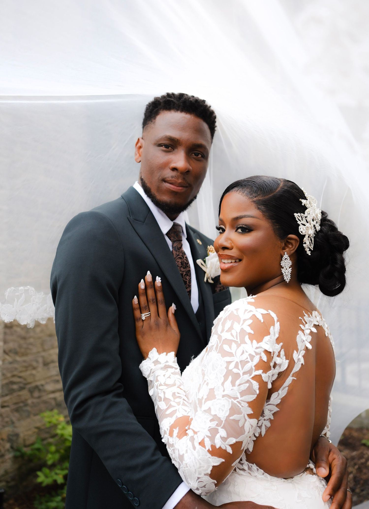 Wedding portrait showing formal couple in bridal attire against white wall with dramatic lighting.