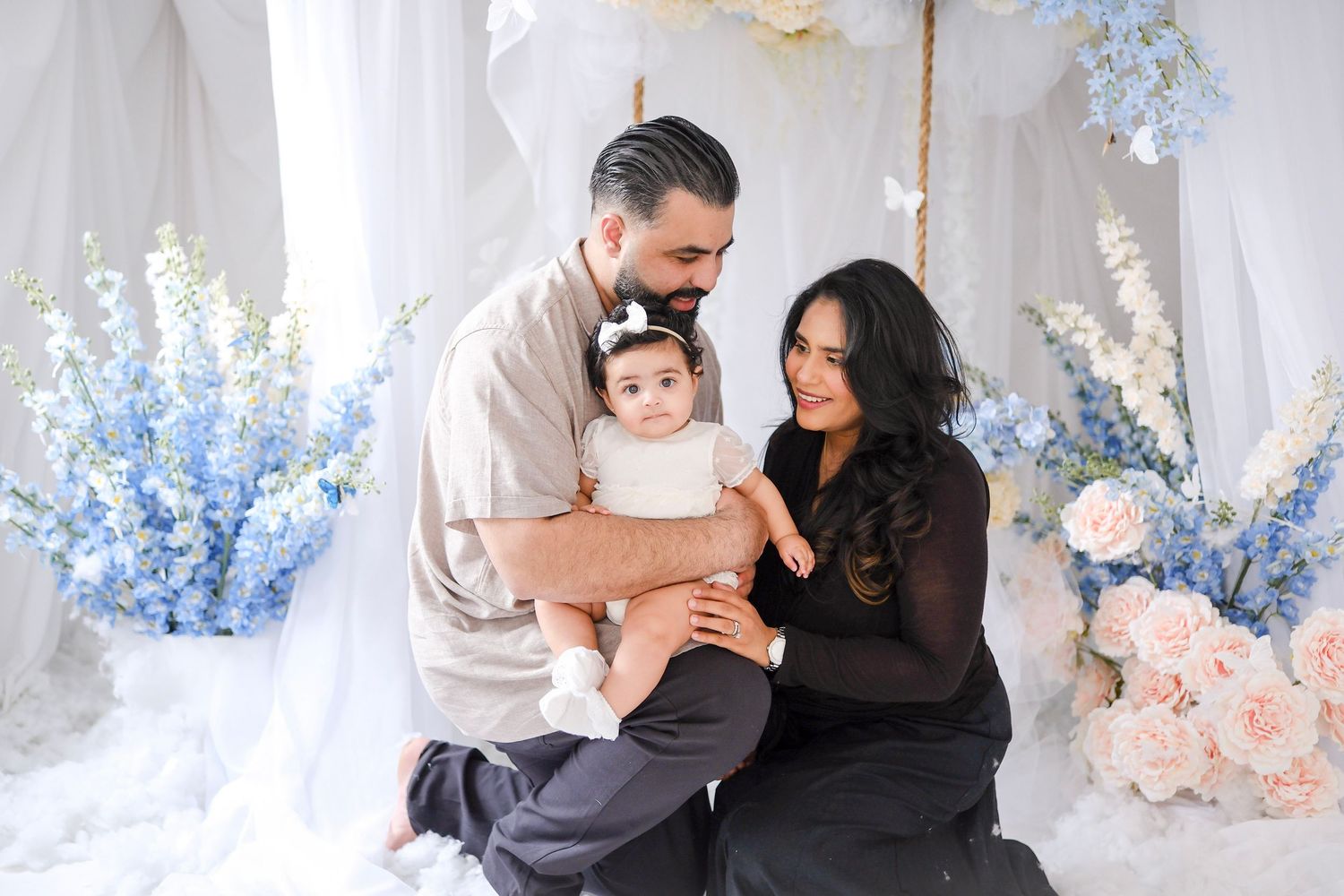 Family portrait with baby against a backdrop of blue and pink floral decorations and white curtains.