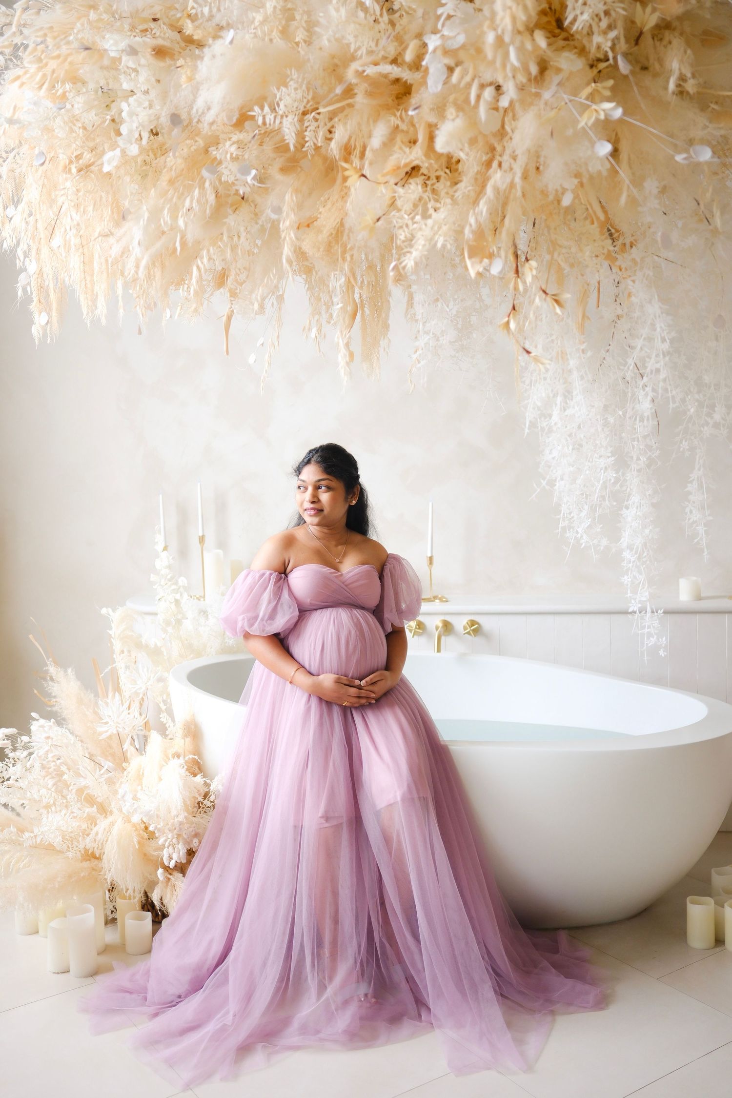 A maternity photoshoot in a luxurious bathroom with flowing pampas grass decor and a pink tulle gown.